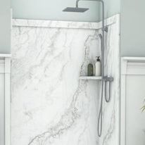 Shower stall with white marble-look walls, silver fixtures, and shelf with toiletries.
