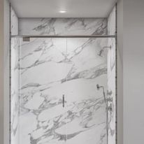 Shower with marble walls, glass doors, and chrome fixtures.