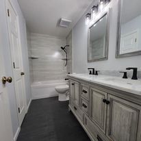 Bathroom with dual sinks, a tub, and a dark floor. White and grey tones dominate.