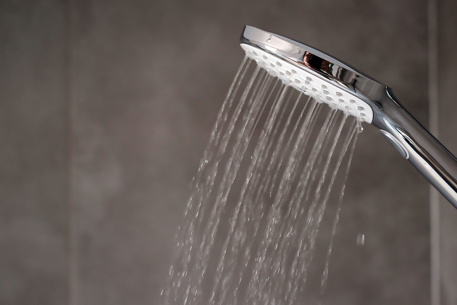 Chrome showerhead spraying water, gray tile background.