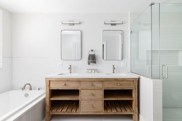 Bathroom with double vanity, mirrors, and shower. Neutral tones, light wood cabinet, white walls, and a bathtub.
