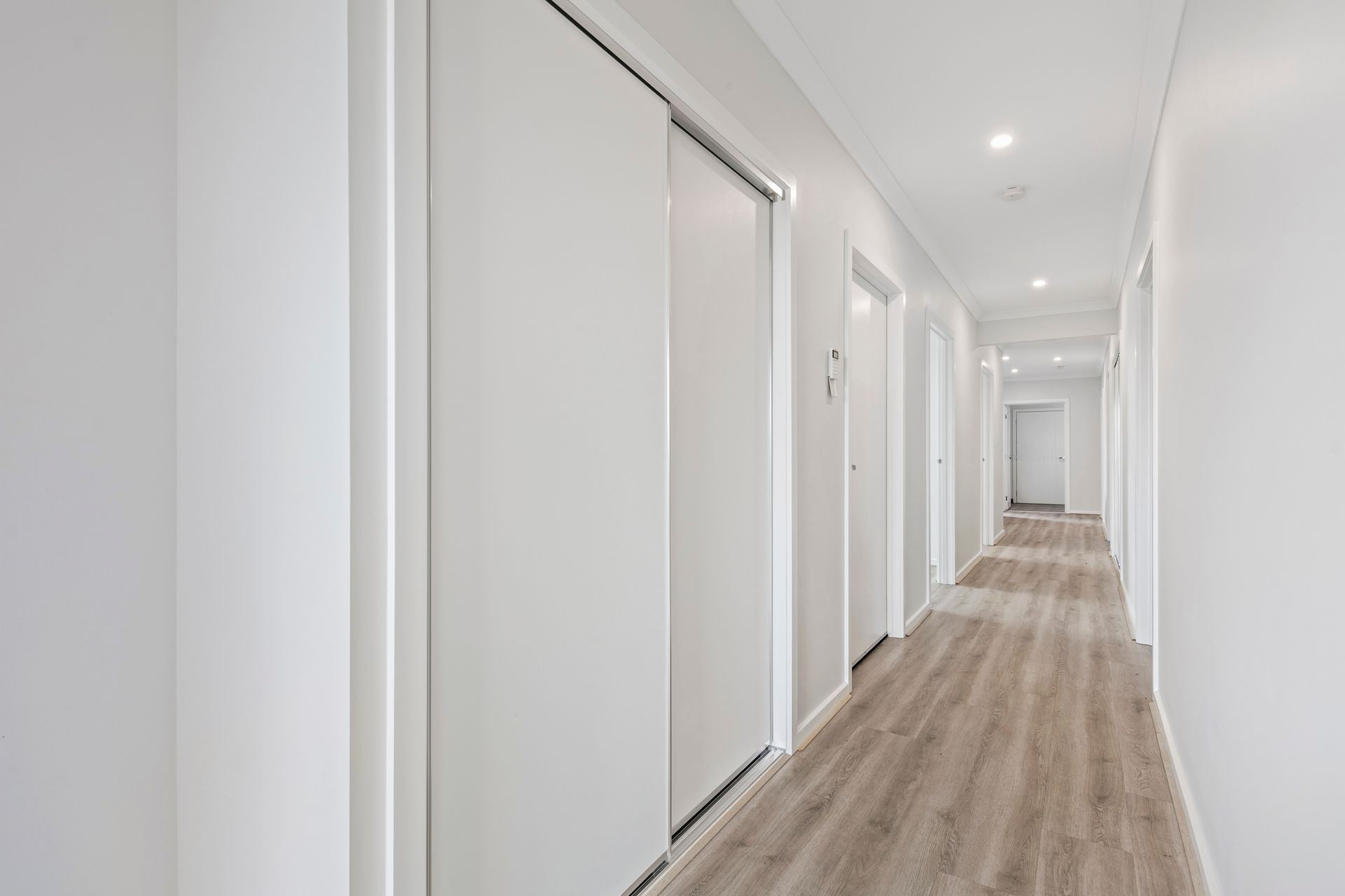 A long hallway with white walls and wooden floors in a house.