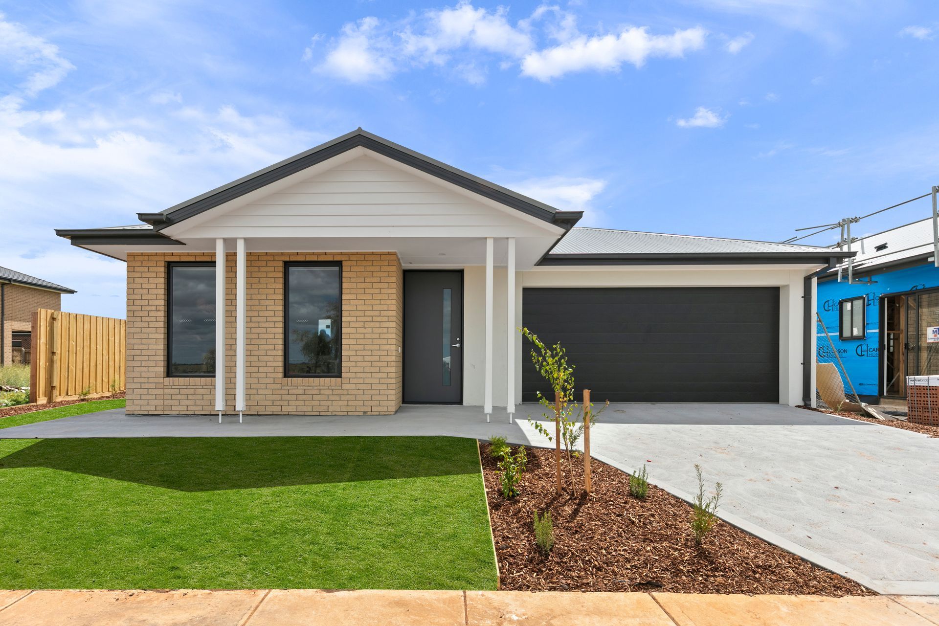 A brick house with a black garage door is being built in a residential area.