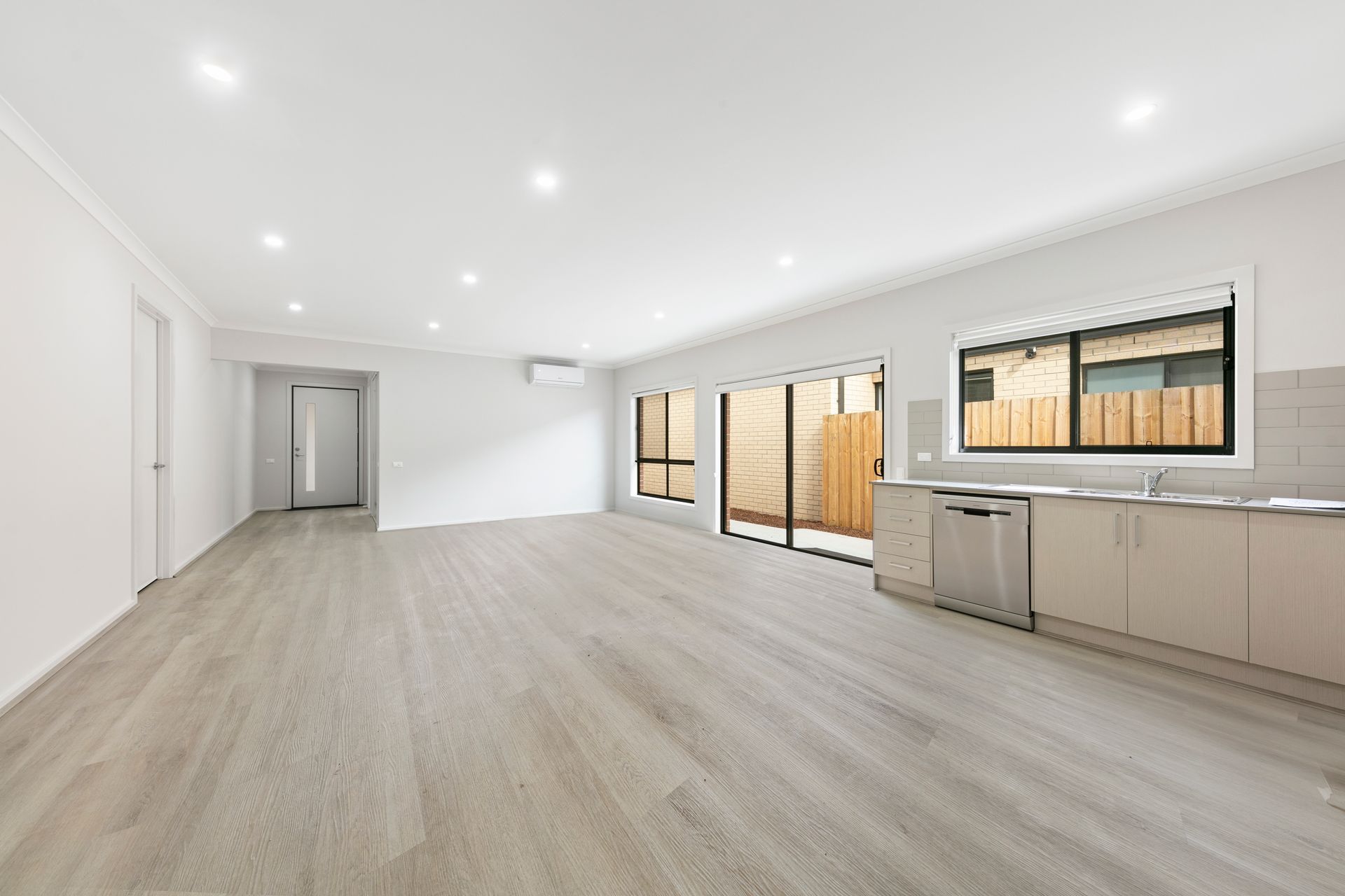 An empty living room with hardwood floors and a kitchen.