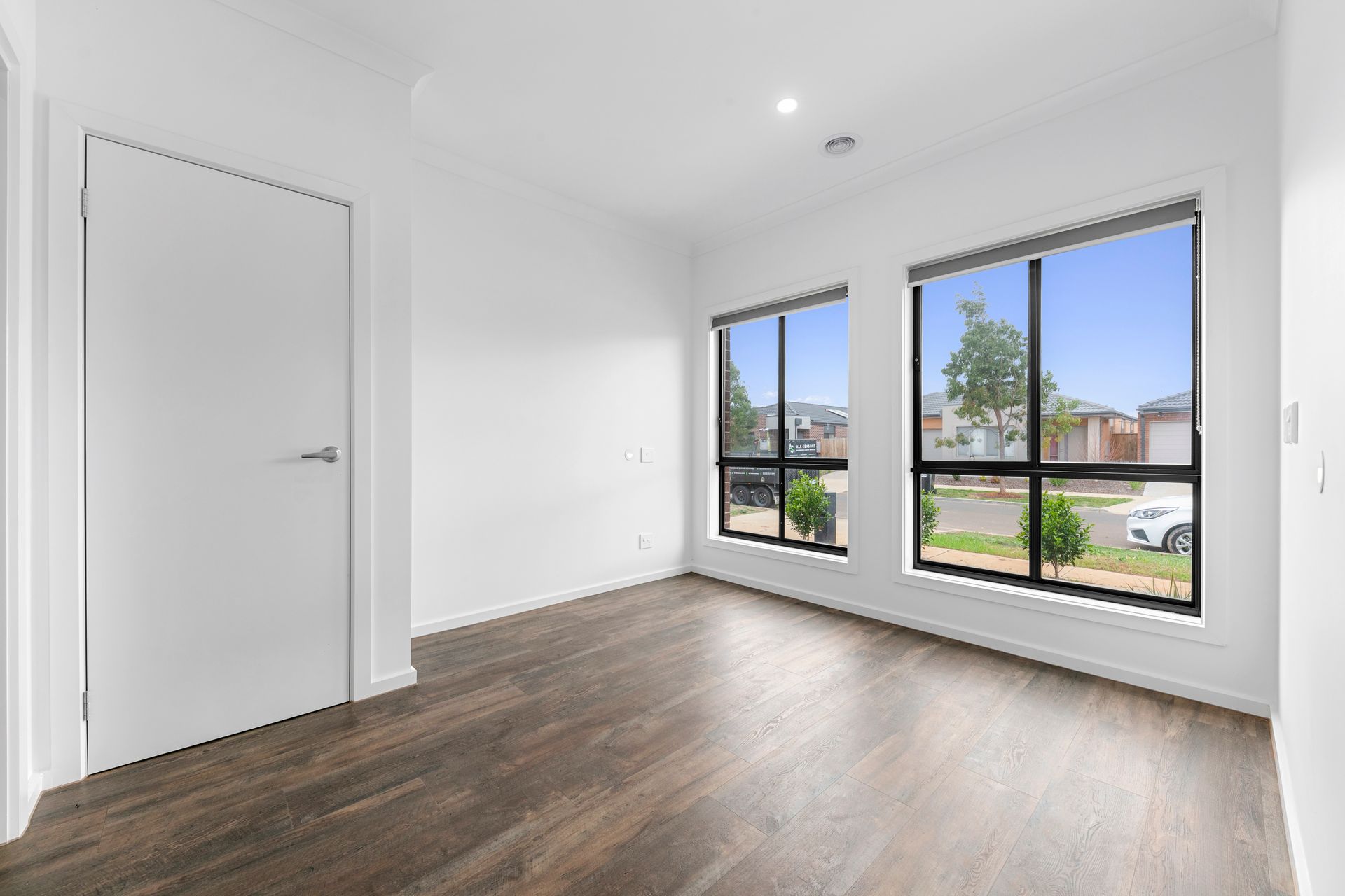 An empty room with hardwood floors and two windows.