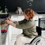 A woman in a wheelchair is using a cell phone in a kitchen.