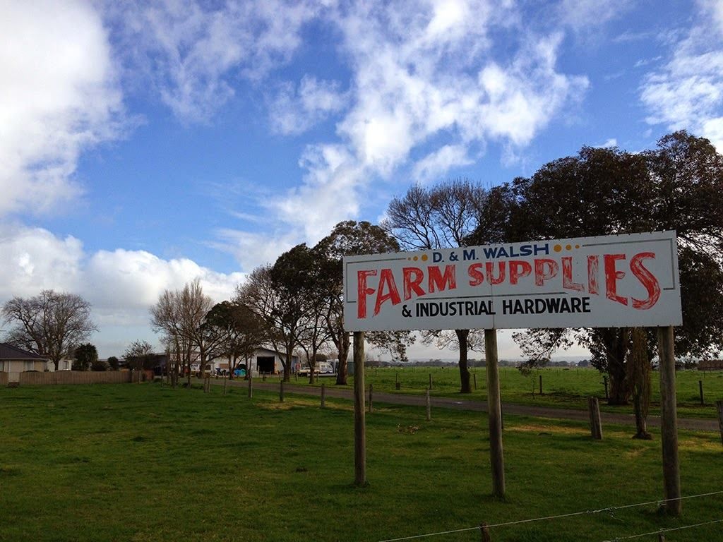A sign for farm supplies and industrial hardware is in a grassy field.