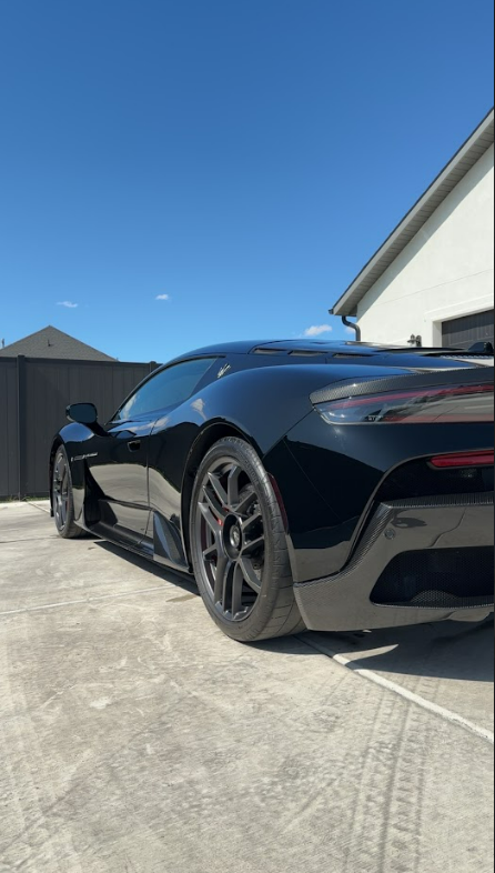 A black sports car is parked in a driveway in front of a house.
