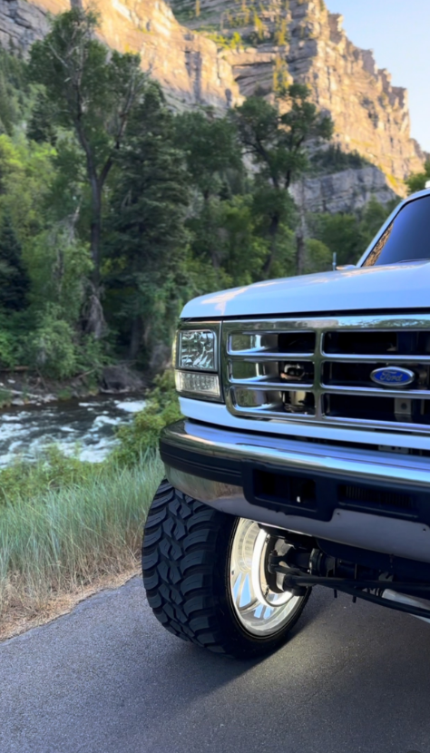 A white truck is parked on the side of a road next to a river.