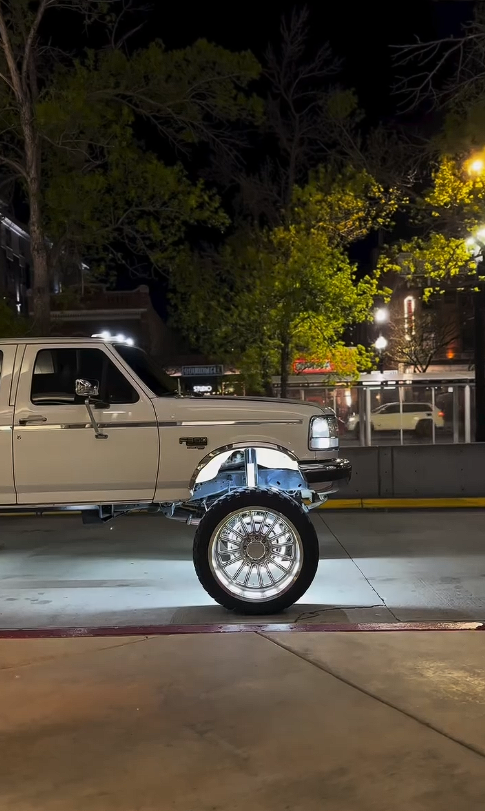 A white truck is parked in a parking lot at night.
