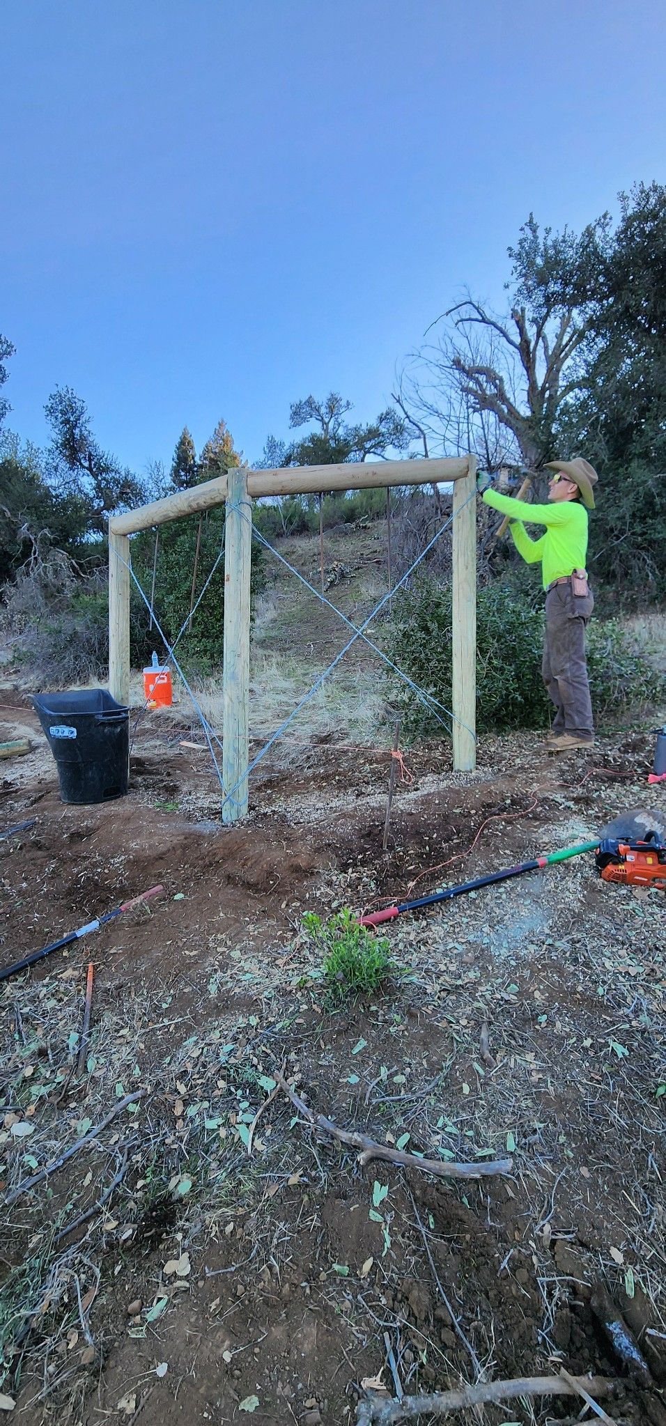 A person in neon green shirt building a fence in an outdoor setting.