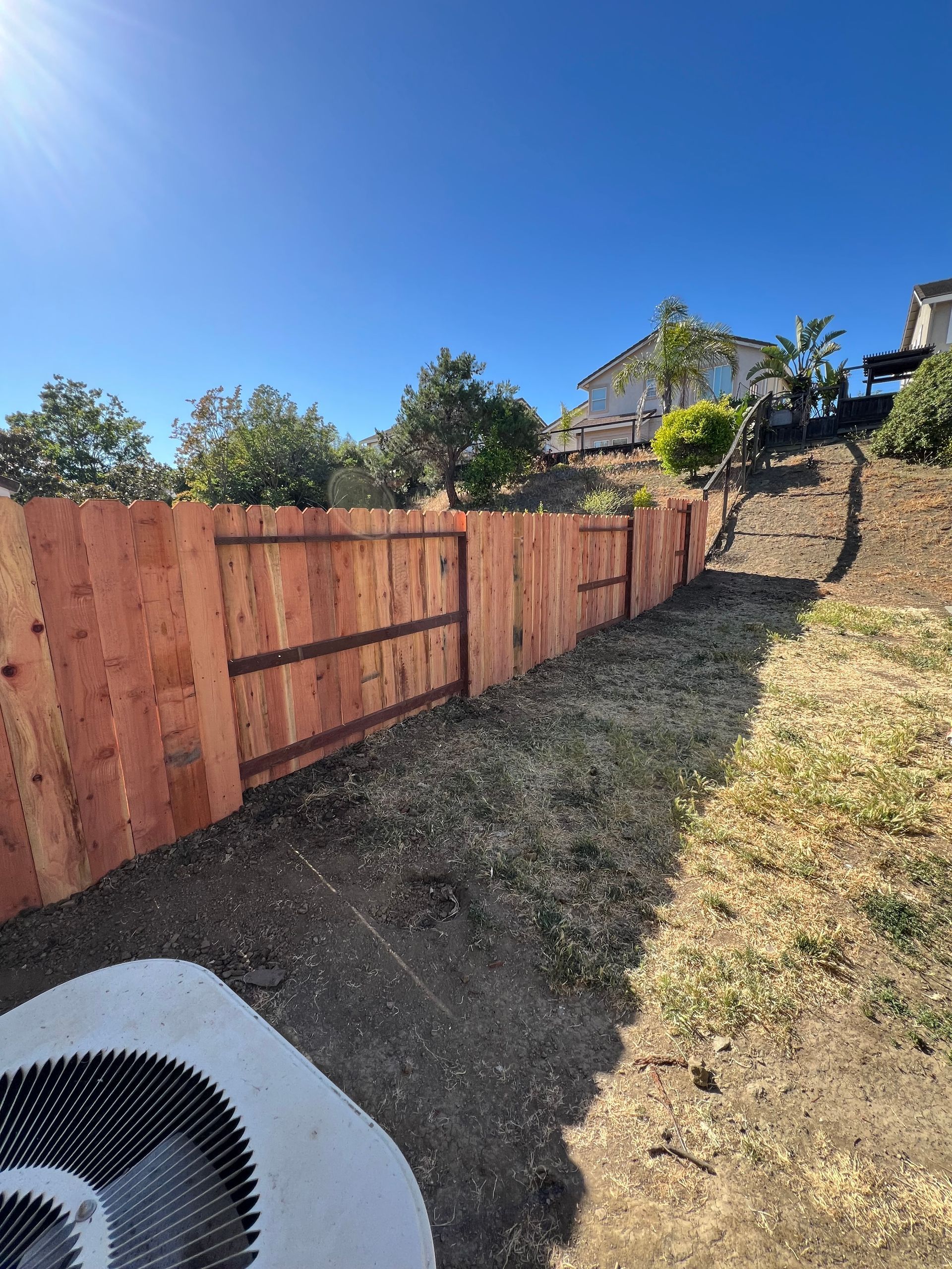 A new wooden fence bordering a sloped, grassy yard on a sunny day.