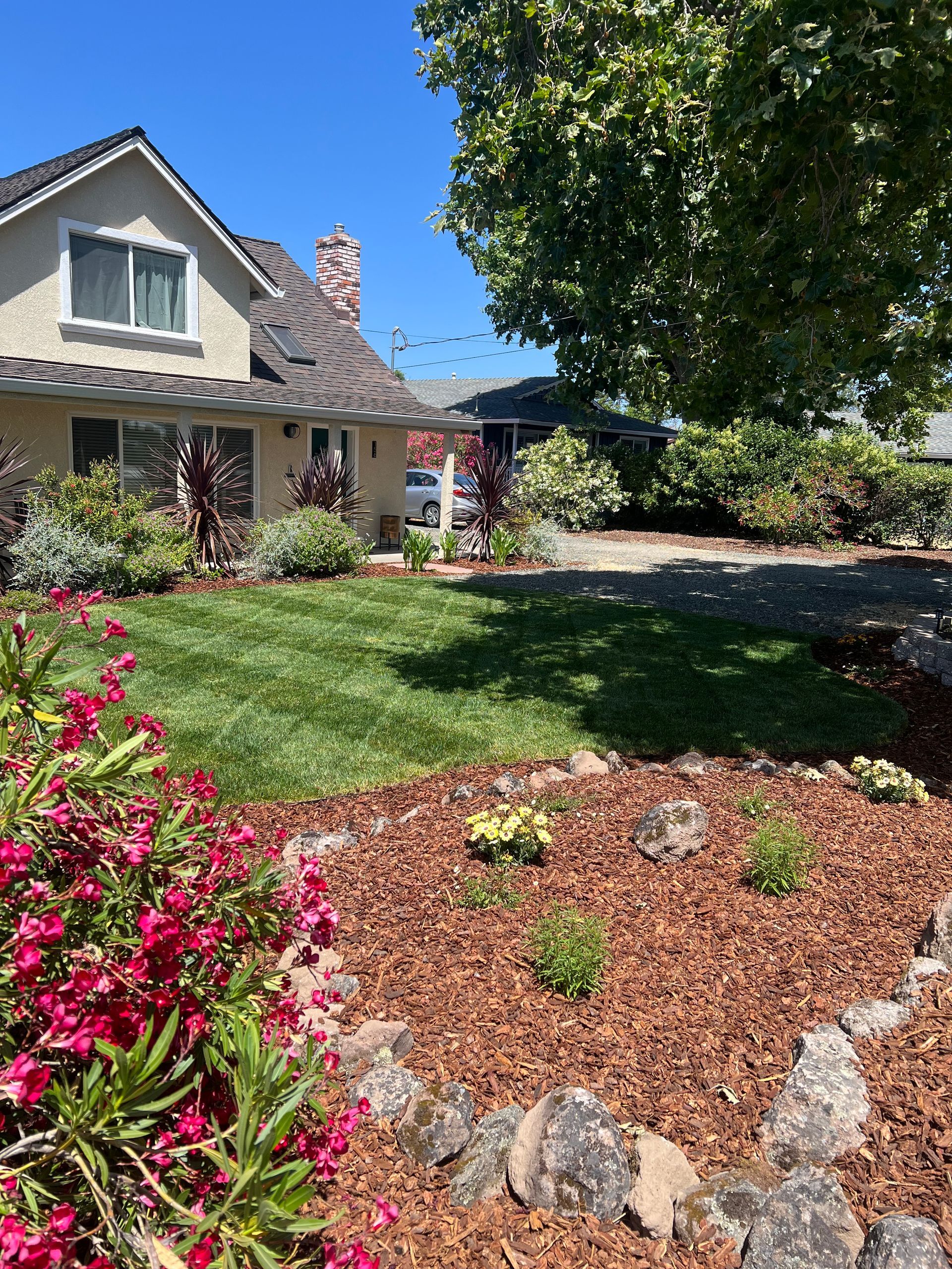 House with well-kept lawn and flower beds, under a bright blue sky.