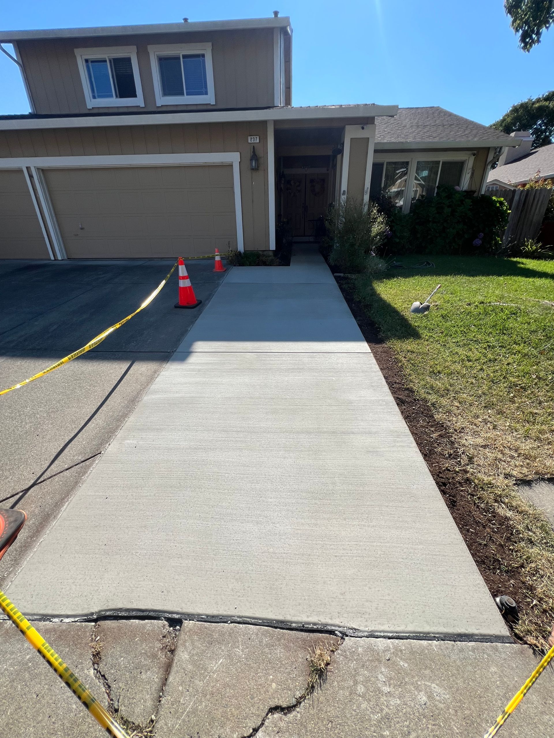 New concrete walkway leading to a two-story house with caution tape and traffic cones.