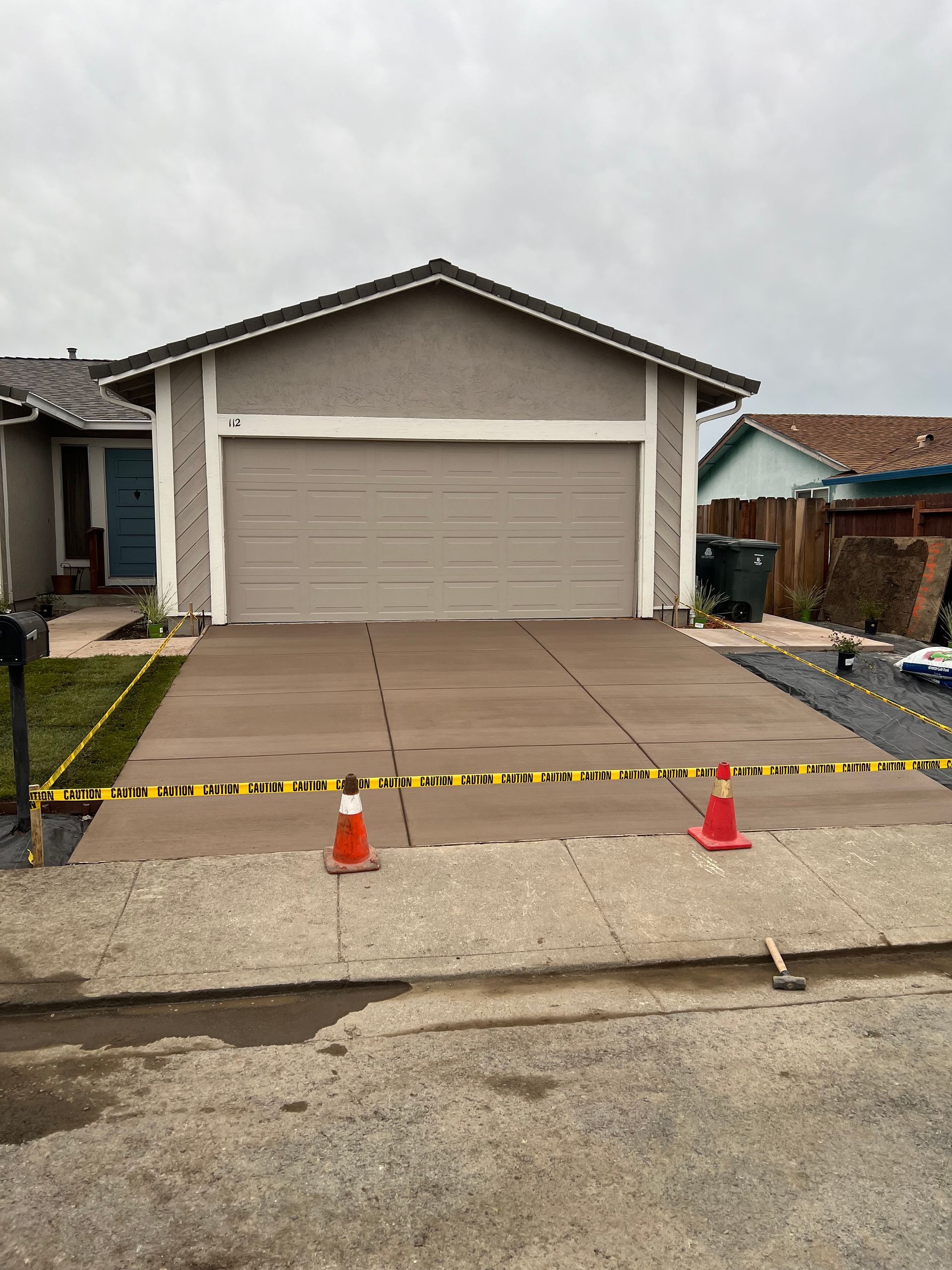 New concrete driveway in front of a tan house with garage, marked with caution tape and cones.