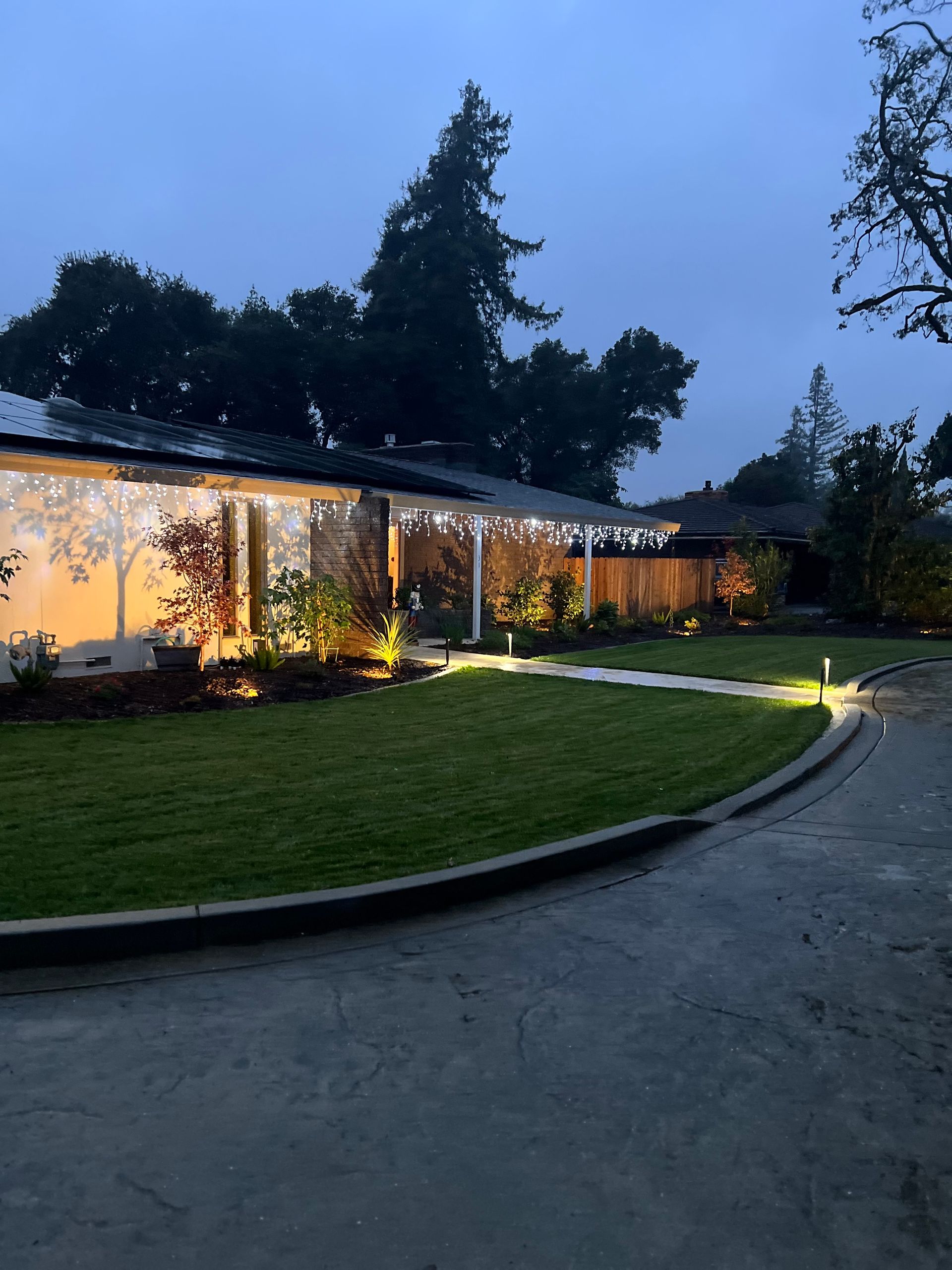 A house at dusk with string lights, a green lawn, and a dark driveway.