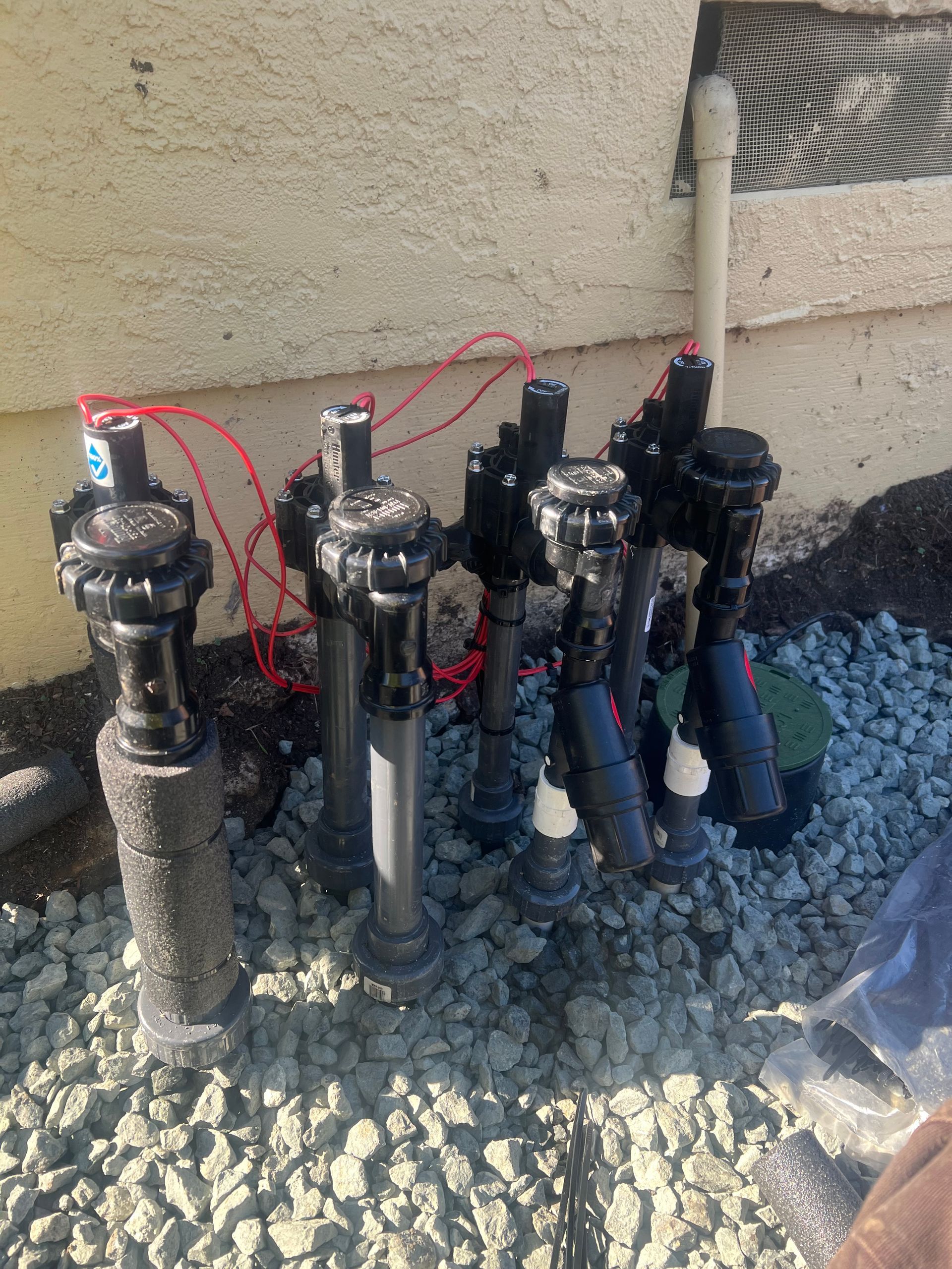 Irrigation system with six valves and wiring against a building with gray gravel.