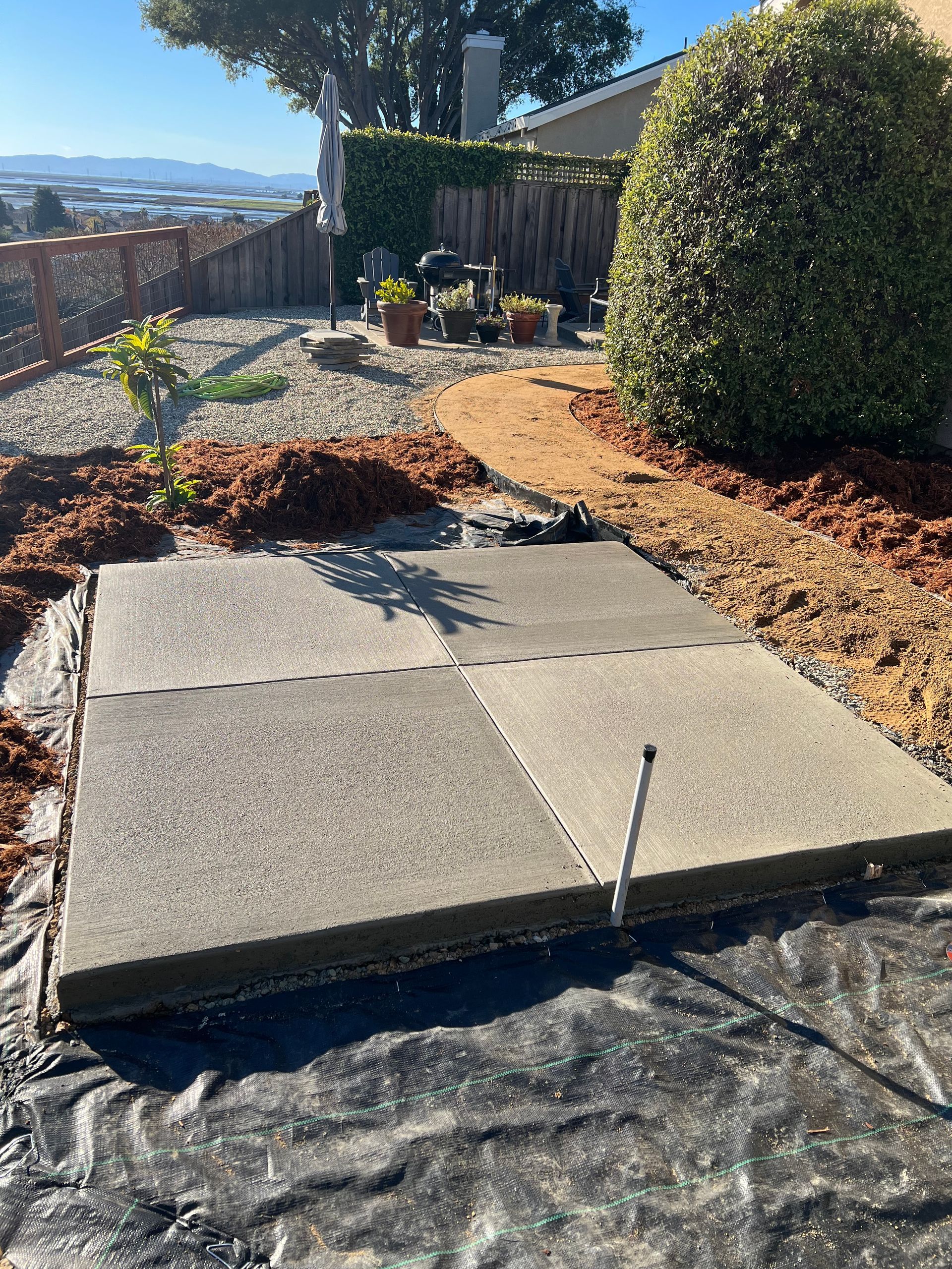 Concrete patio in a yard, surrounded by mulch and landscaping.