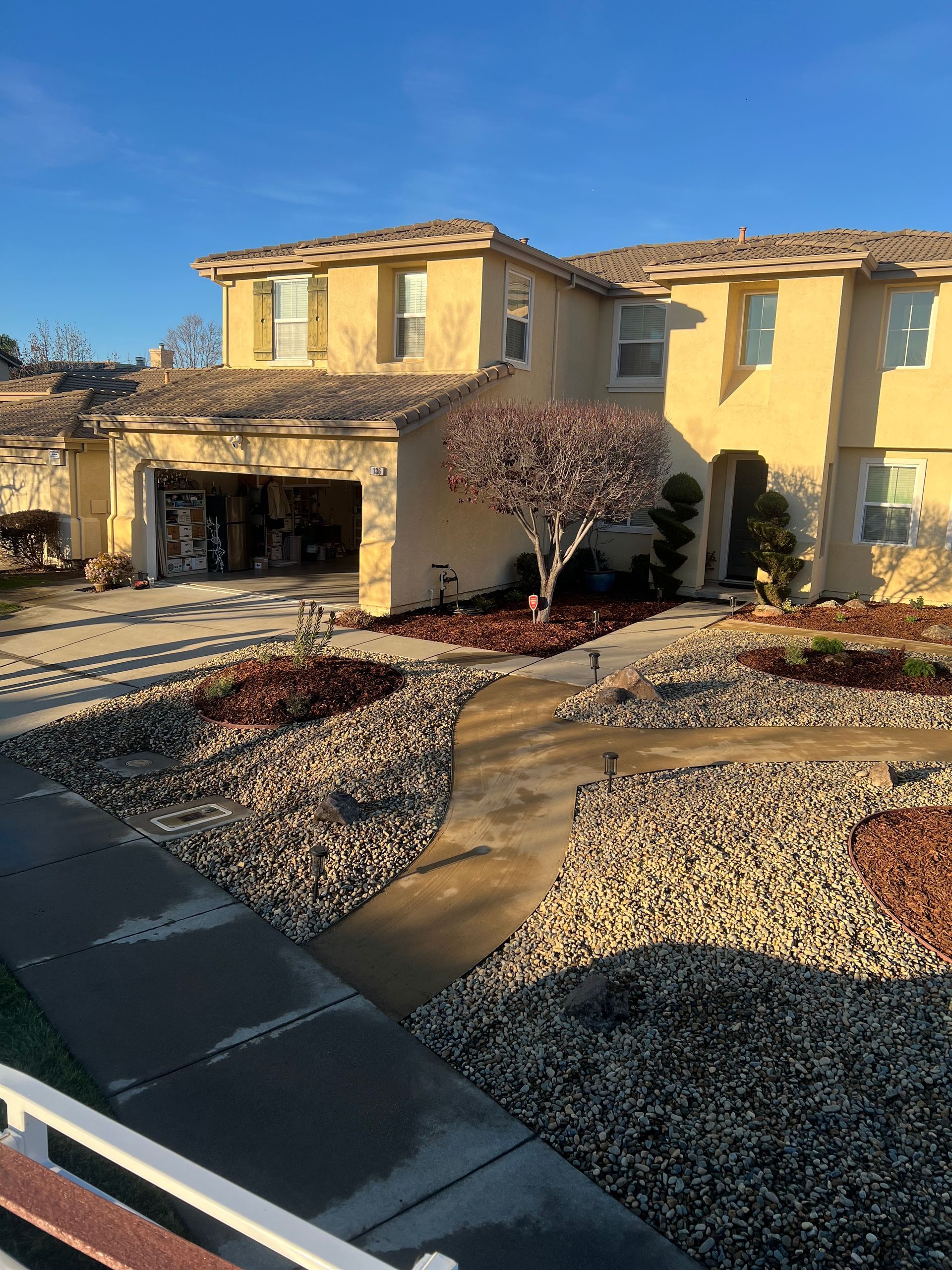 Two-story beige house with a winding path through rock landscaping on a sunny day.