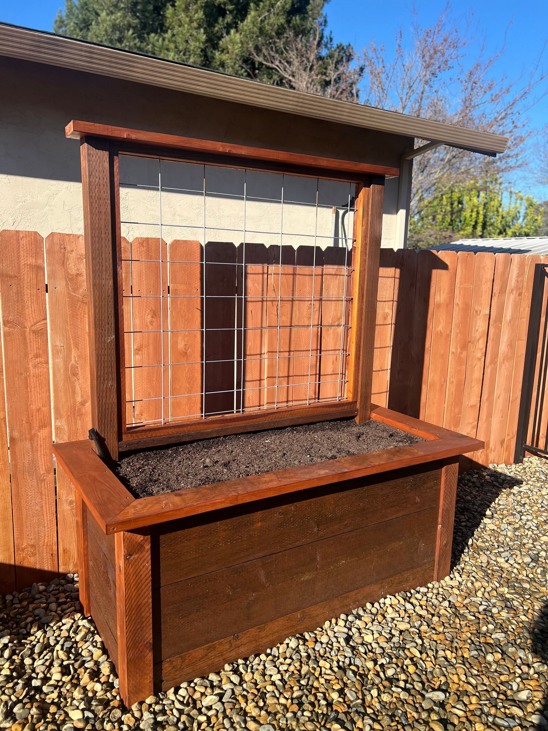 Wooden planter box with trellis, stained brown, outdoors in front of a fence.