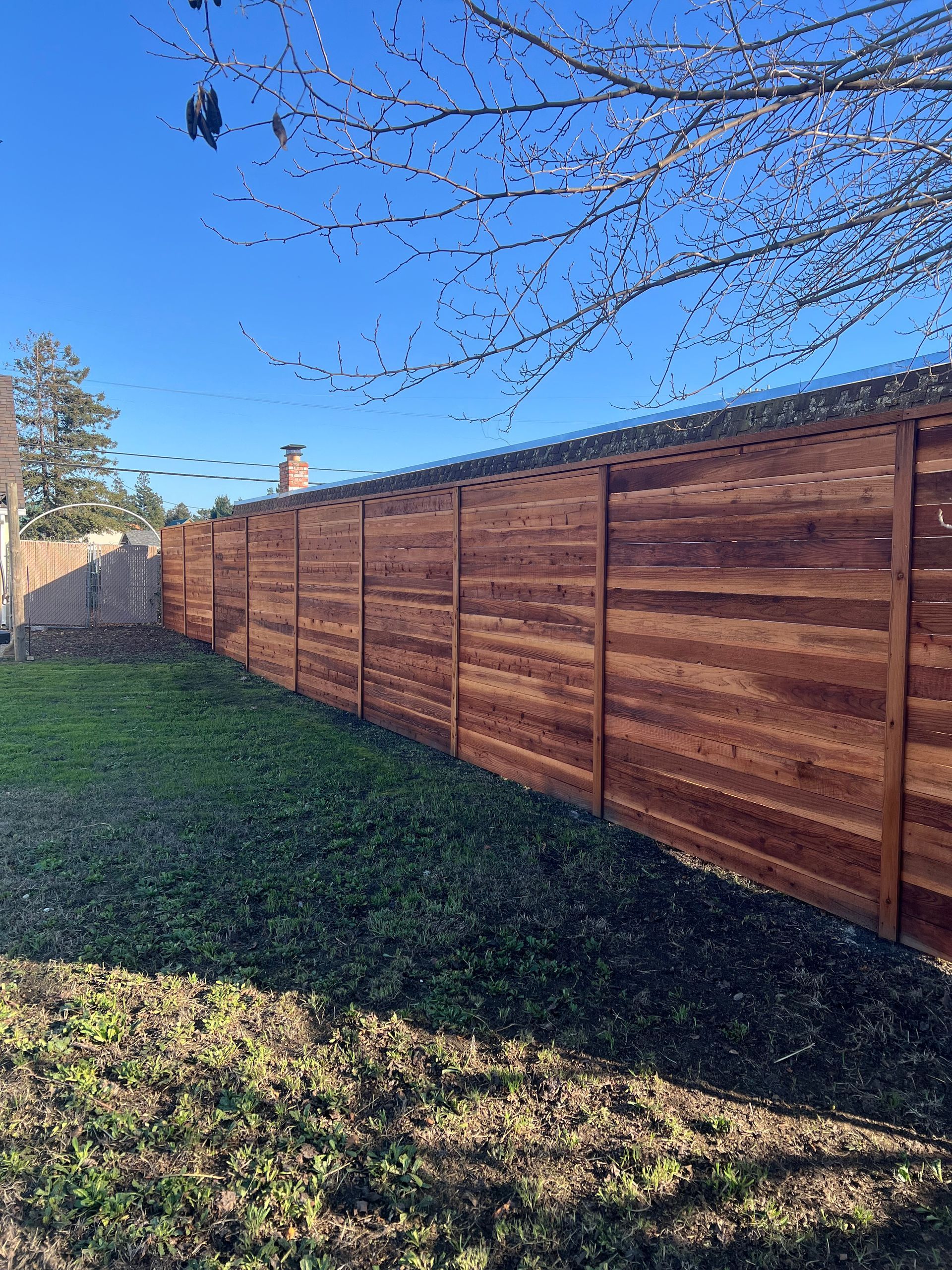Wooden privacy fence in a backyard with green grass and a bright blue sky.
