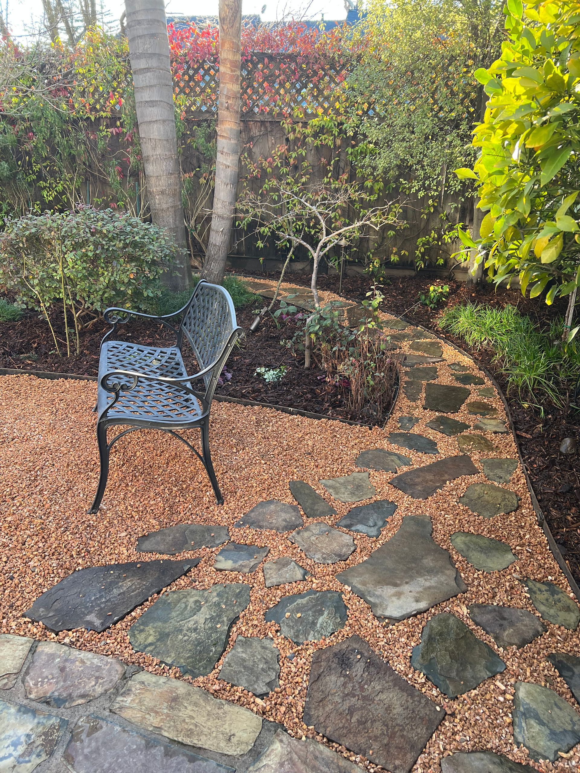 Stone path curves through a garden with a decorative bench. Bark mulch surrounds the path.