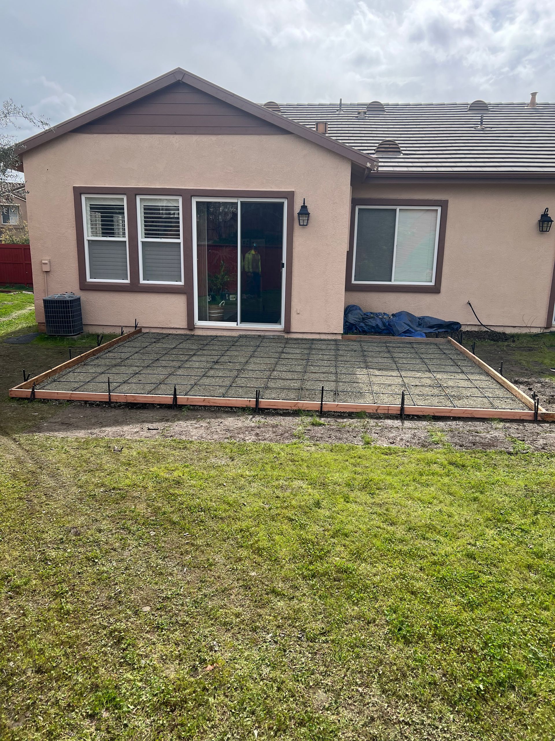 Backyard patio under construction with concrete forms, adjacent to a tan house.
