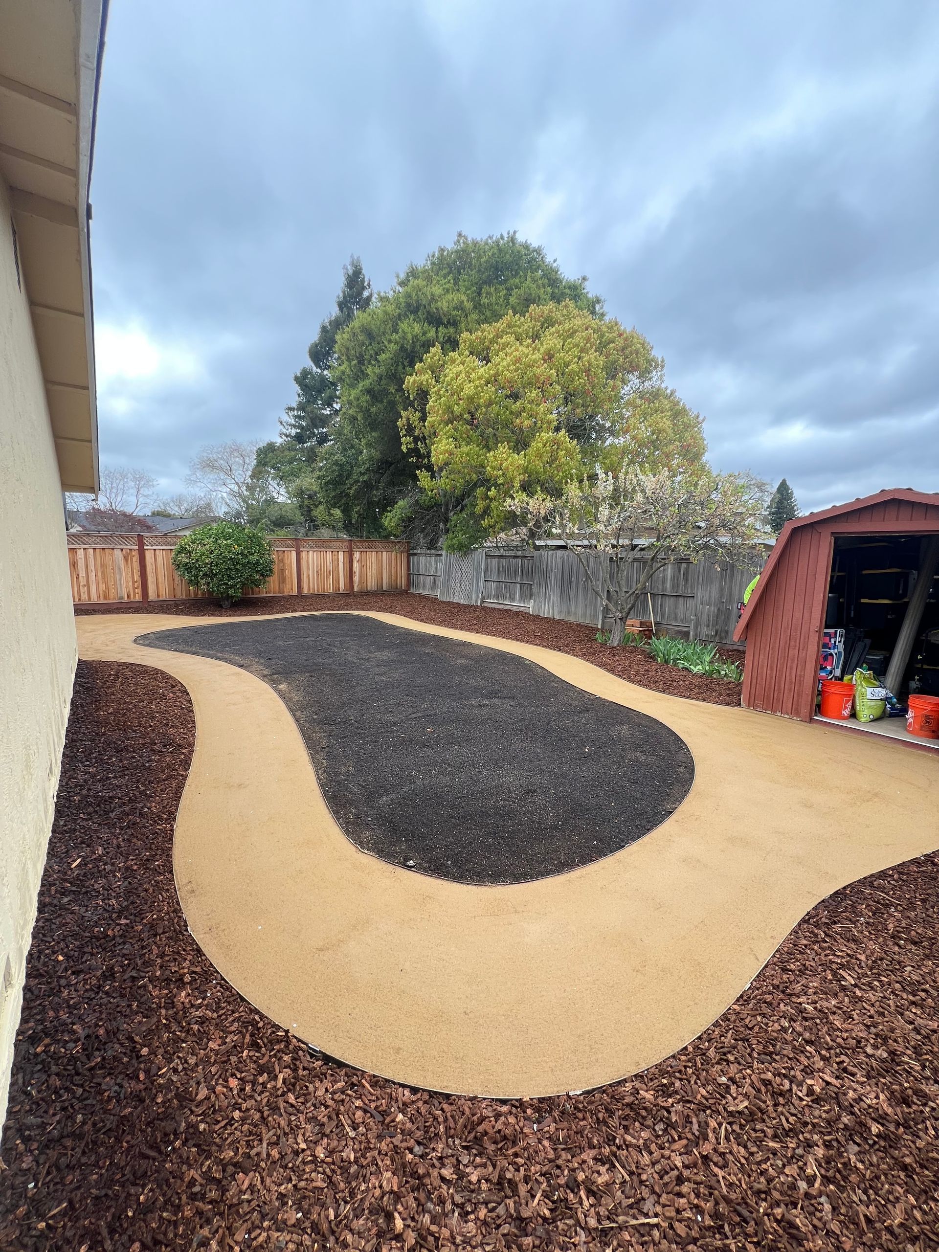 Backyard with a path, mulch, and a shed, under a cloudy sky.