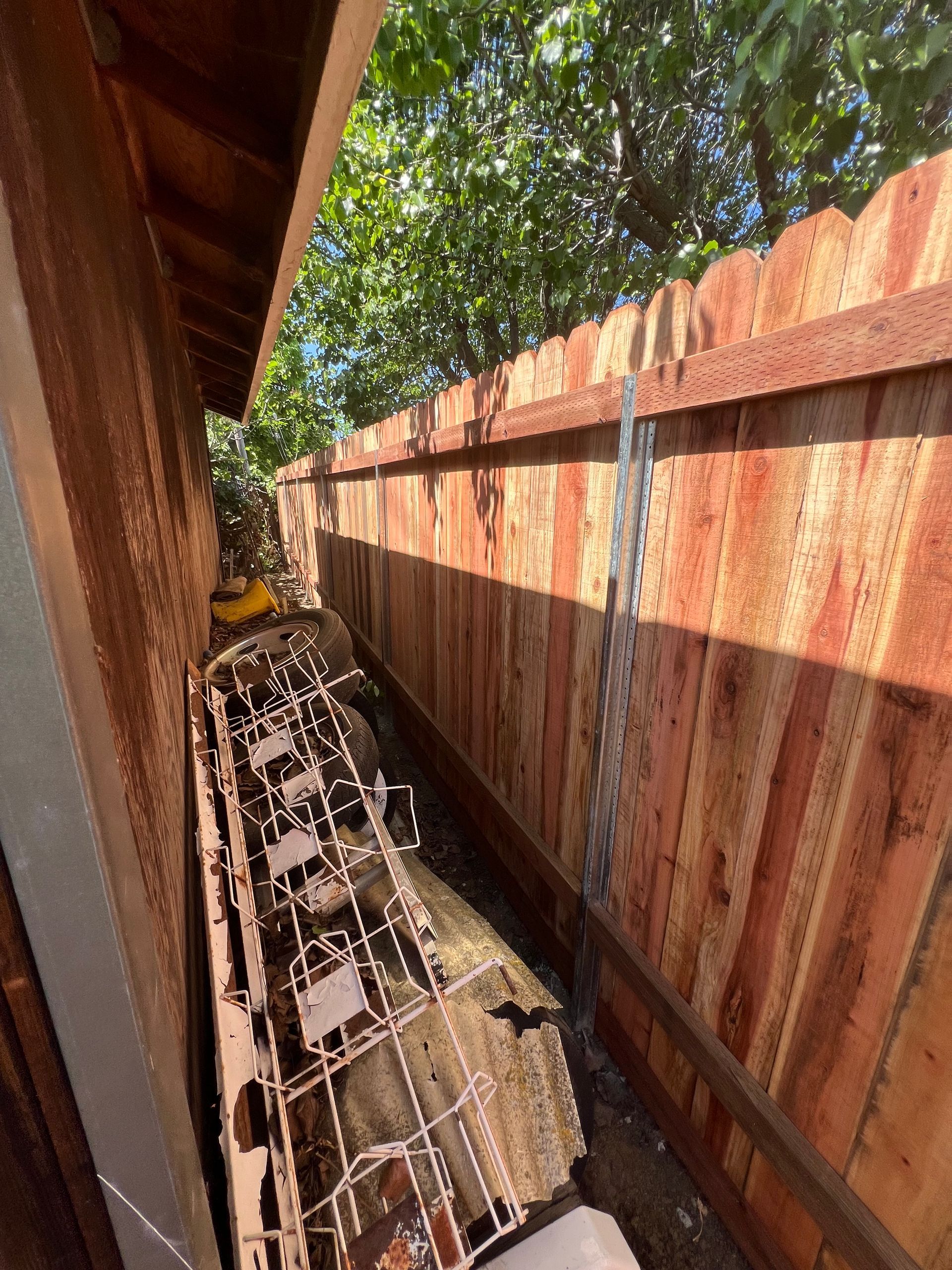 Narrow space between a wooden fence and a building, filled with metal debris.