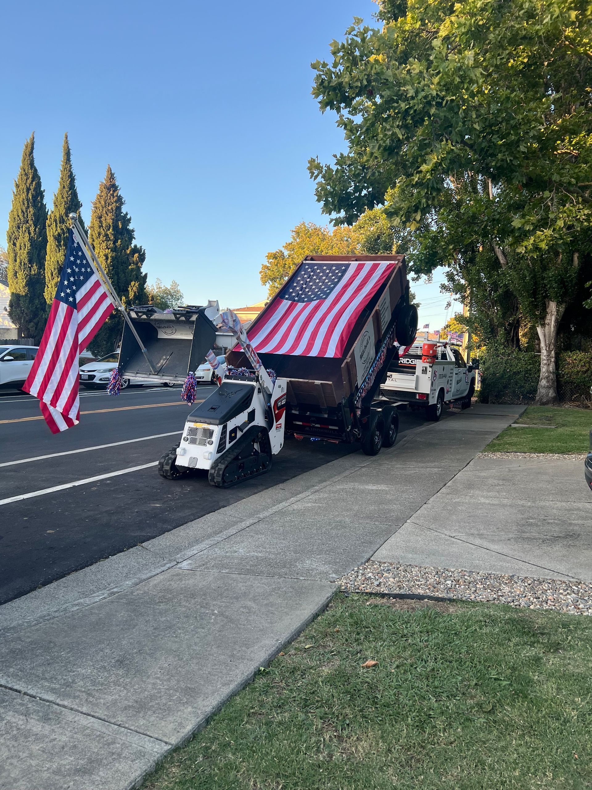 Truck with a large American flag draped over the bed, parked on a street. Another flag waves on the side.