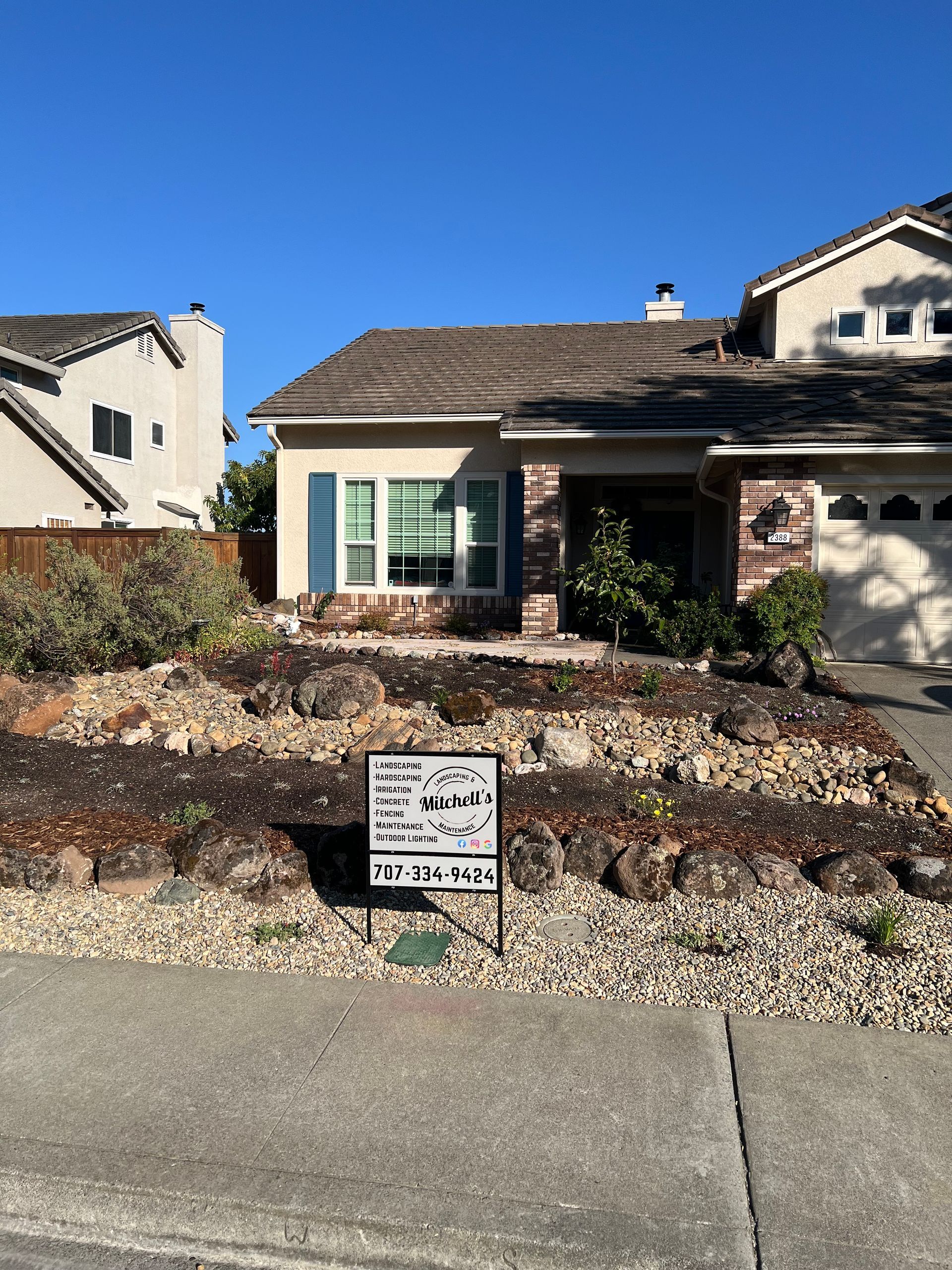 House exterior with blue shutters, brown roof, and dry landscaping. A sign is in front.
