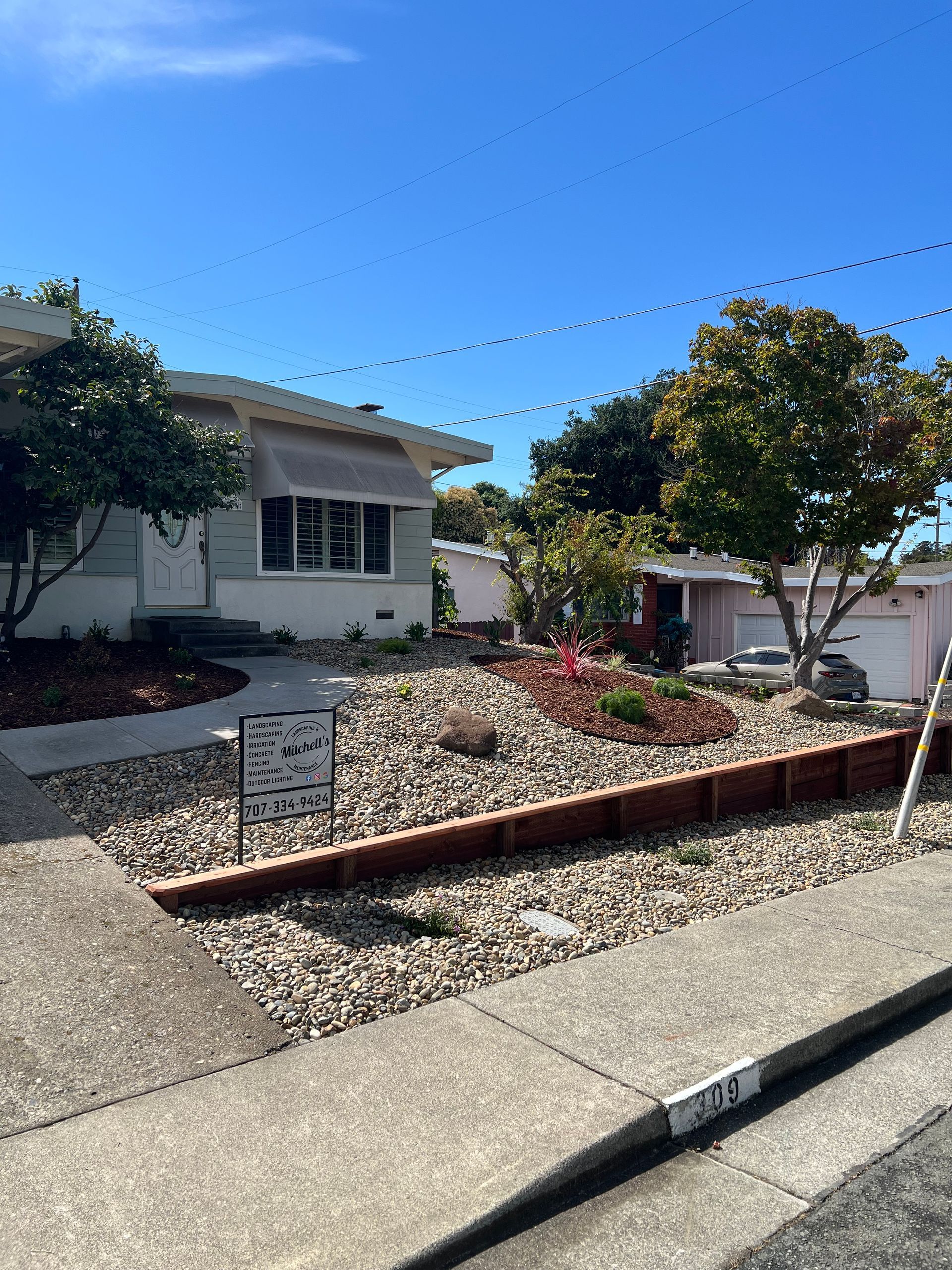 Front yard of a house with brown mulch, rocks, and landscaping. Clear sky overhead.