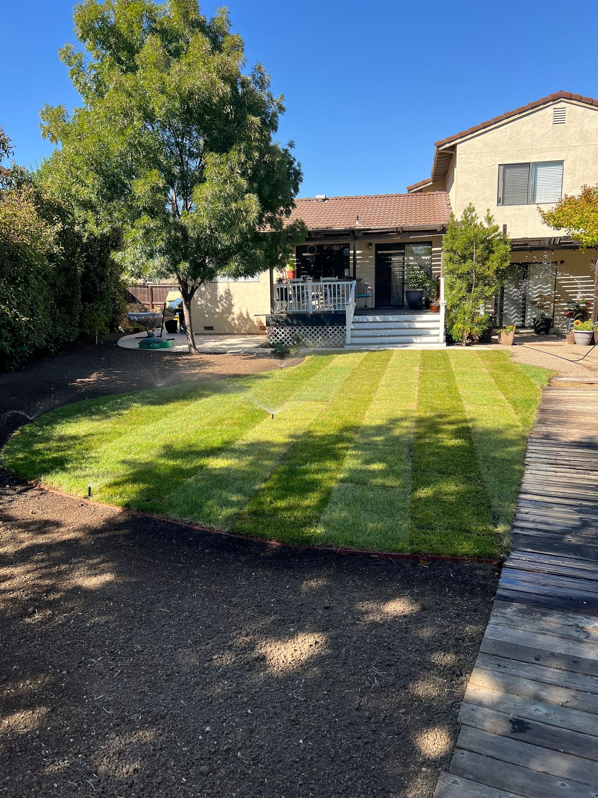 Green lawn with freshly cut stripes in backyard of a two-story house under a blue sky.