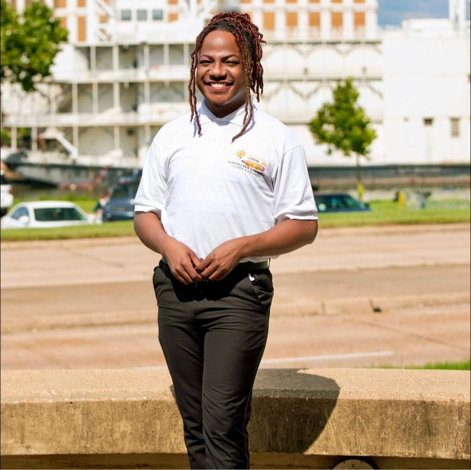 A man with dreadlocks wearing a white shirt and black pants