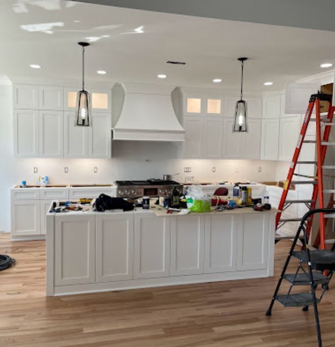 A kitchen under construction with white cabinets and a ladder