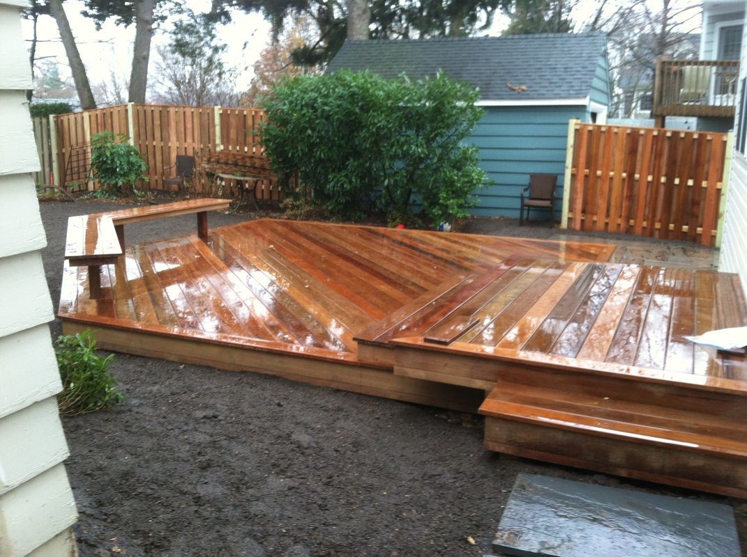 A wooden deck with a bench and stairs in a backyard