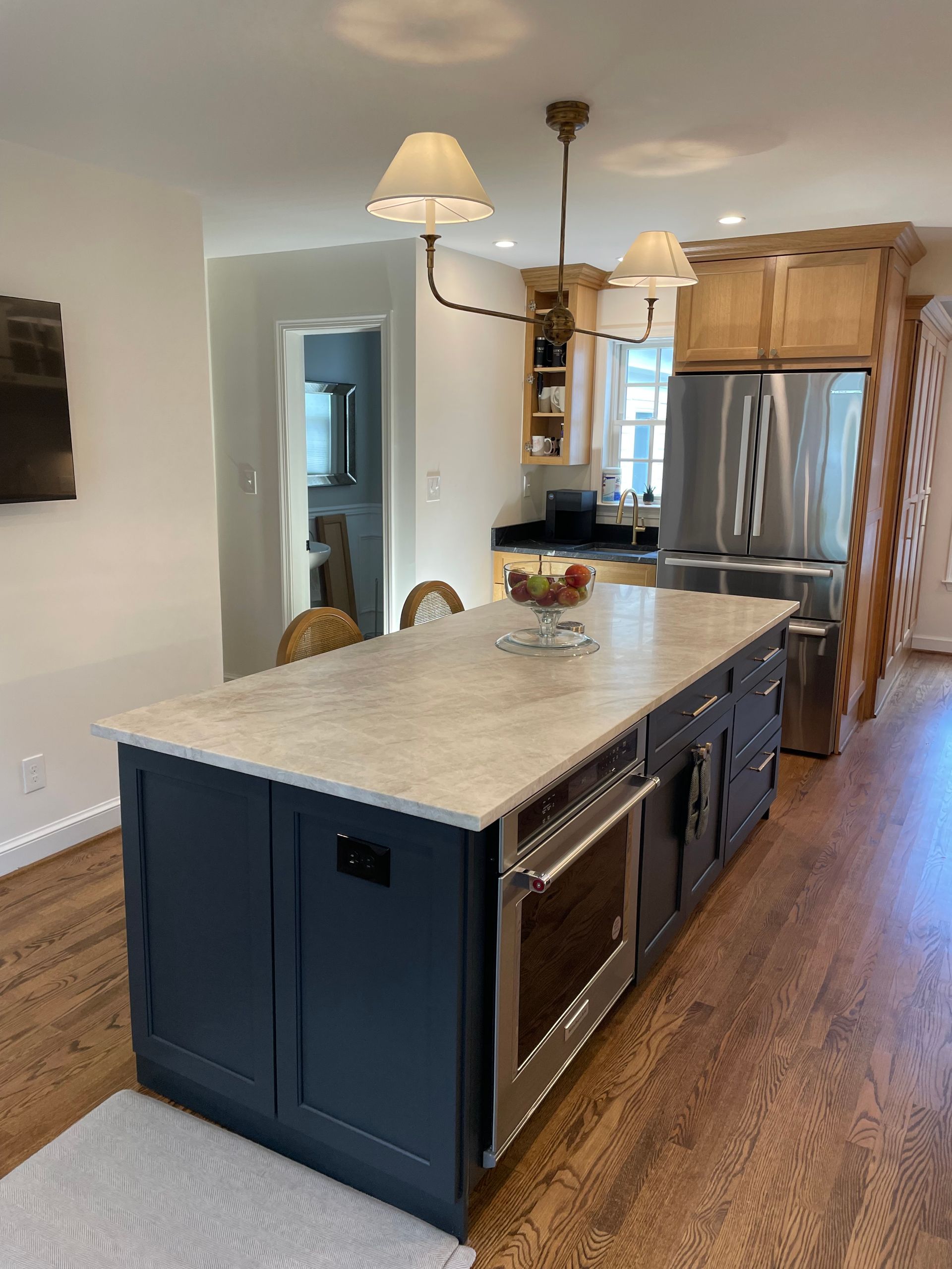 Kitchen with blue island, stainless steel appliances, light wood cabinets, and hardwood floors.