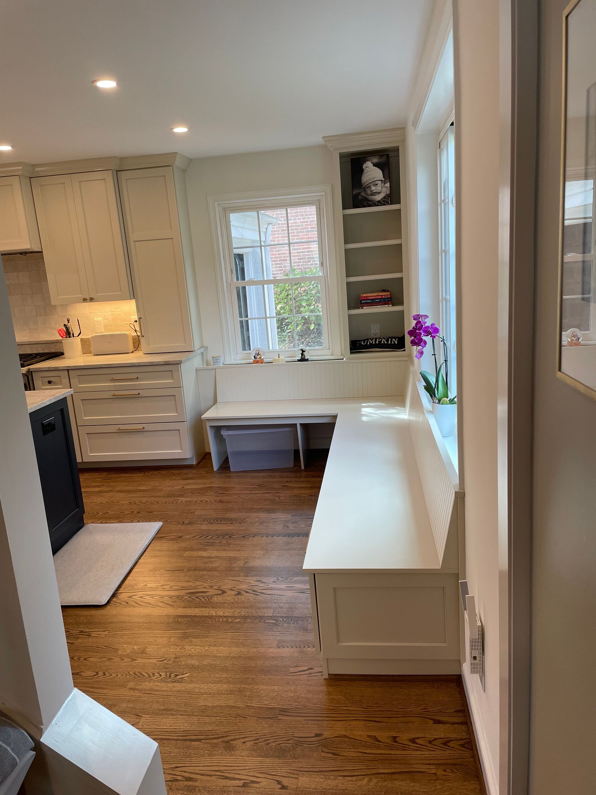 Hardwood floor kitchen with built-in bench seating, cabinets, and a window with shelves.