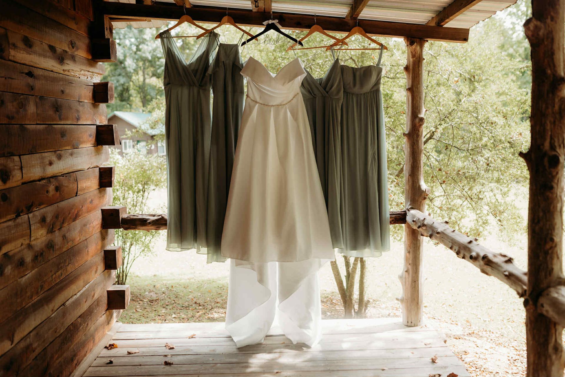 Wedding dress and bridesmaid dresses hanging on a porch rail.