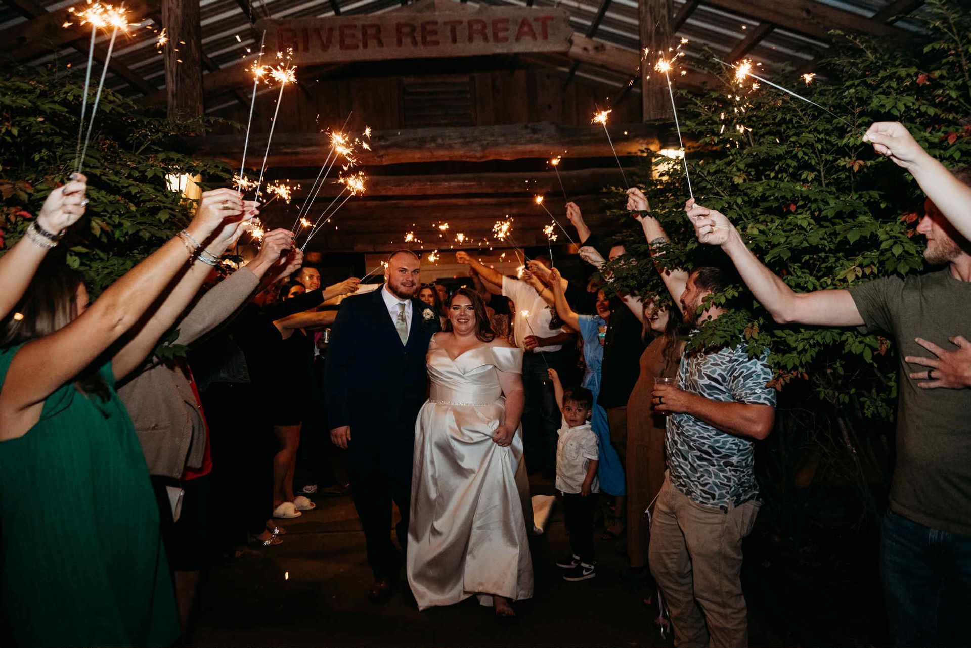 Bride and groom walk under sparklers held by guests at a
