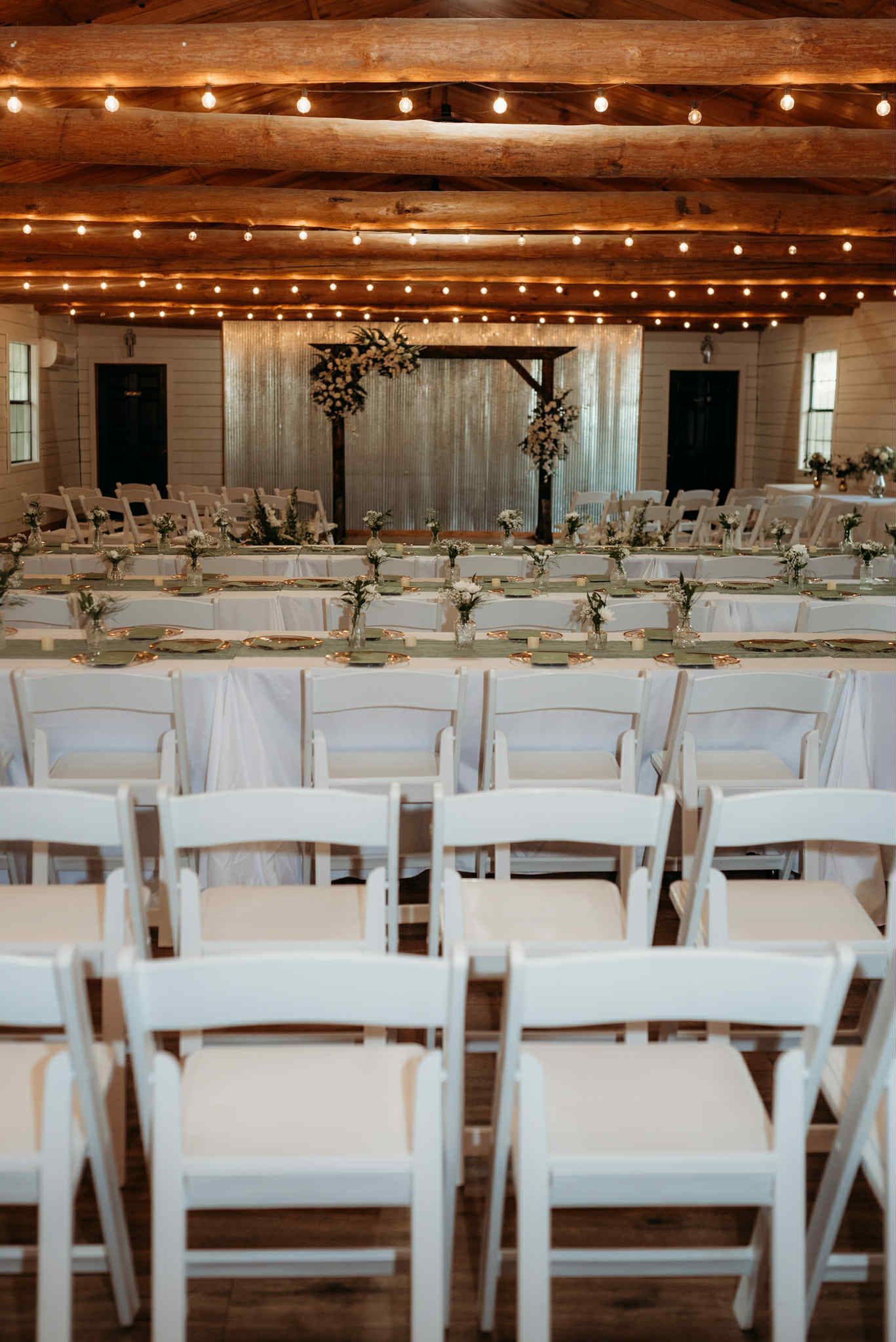 Wedding reception venue with rows of white chairs facing a decorated altar, tables set for guests.