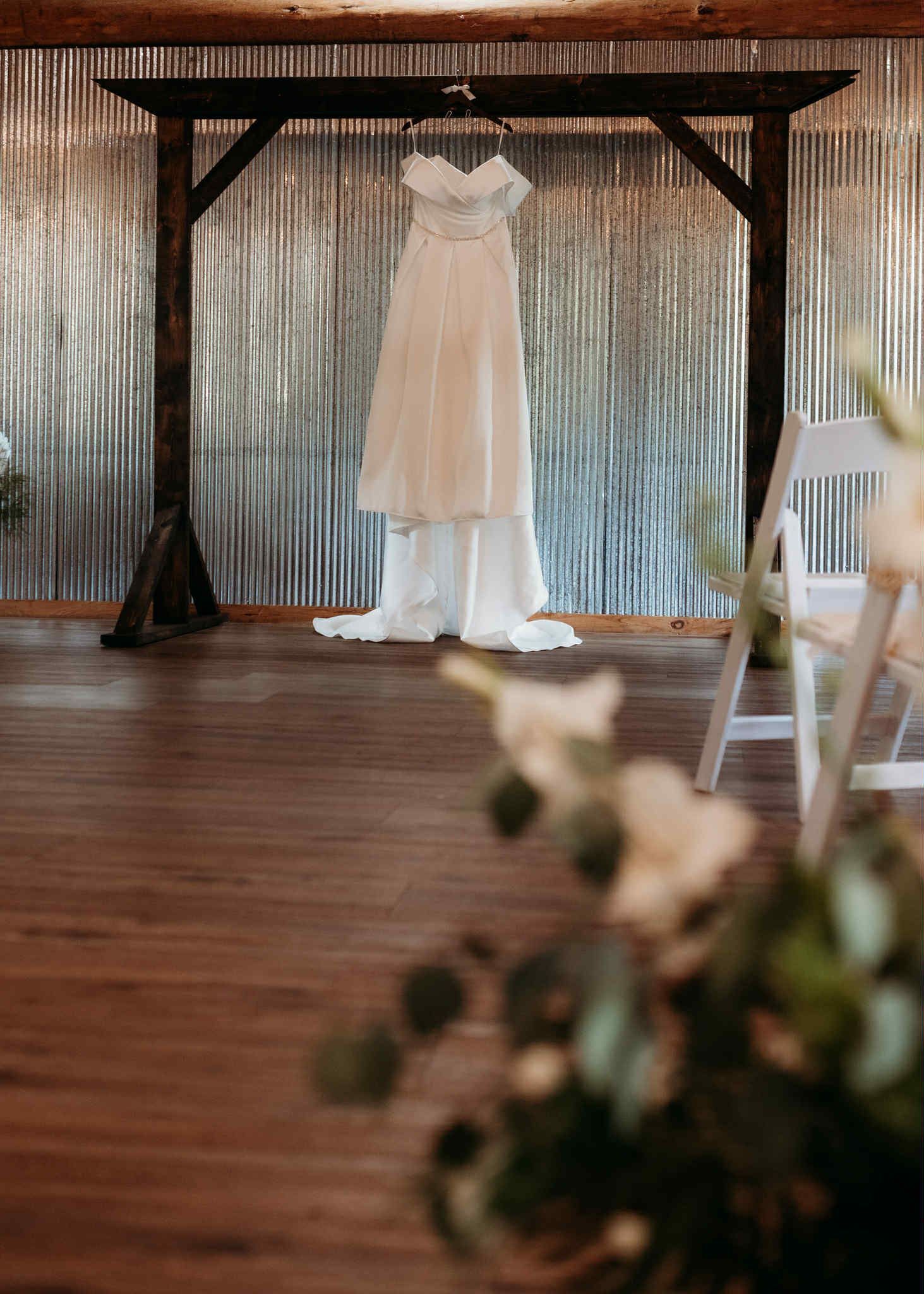 Wedding dress hanging on a wooden arch, against a corrugated metal wall.