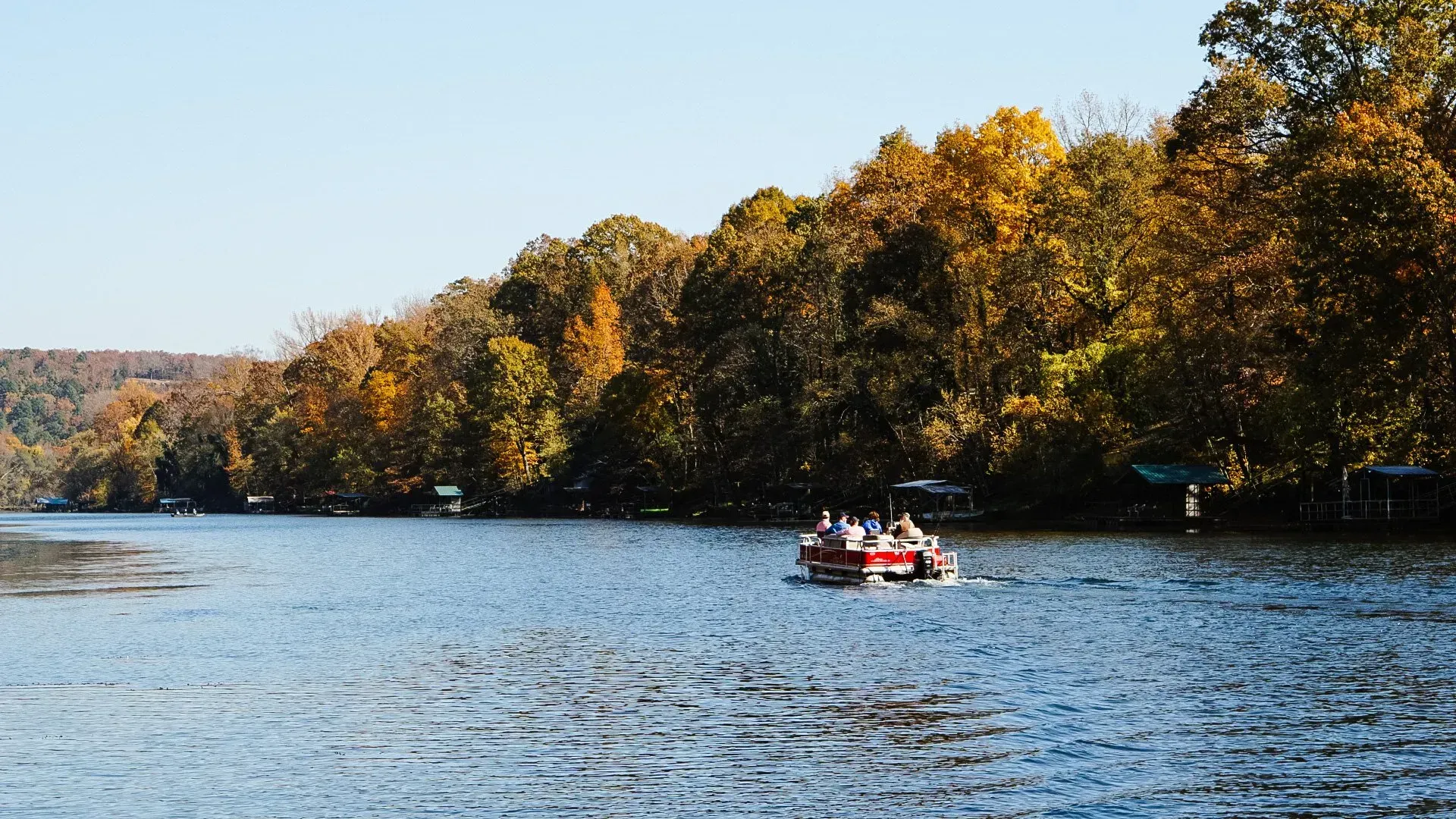 Red boat with people on a dark green lake, surrounded by a forest of green trees.