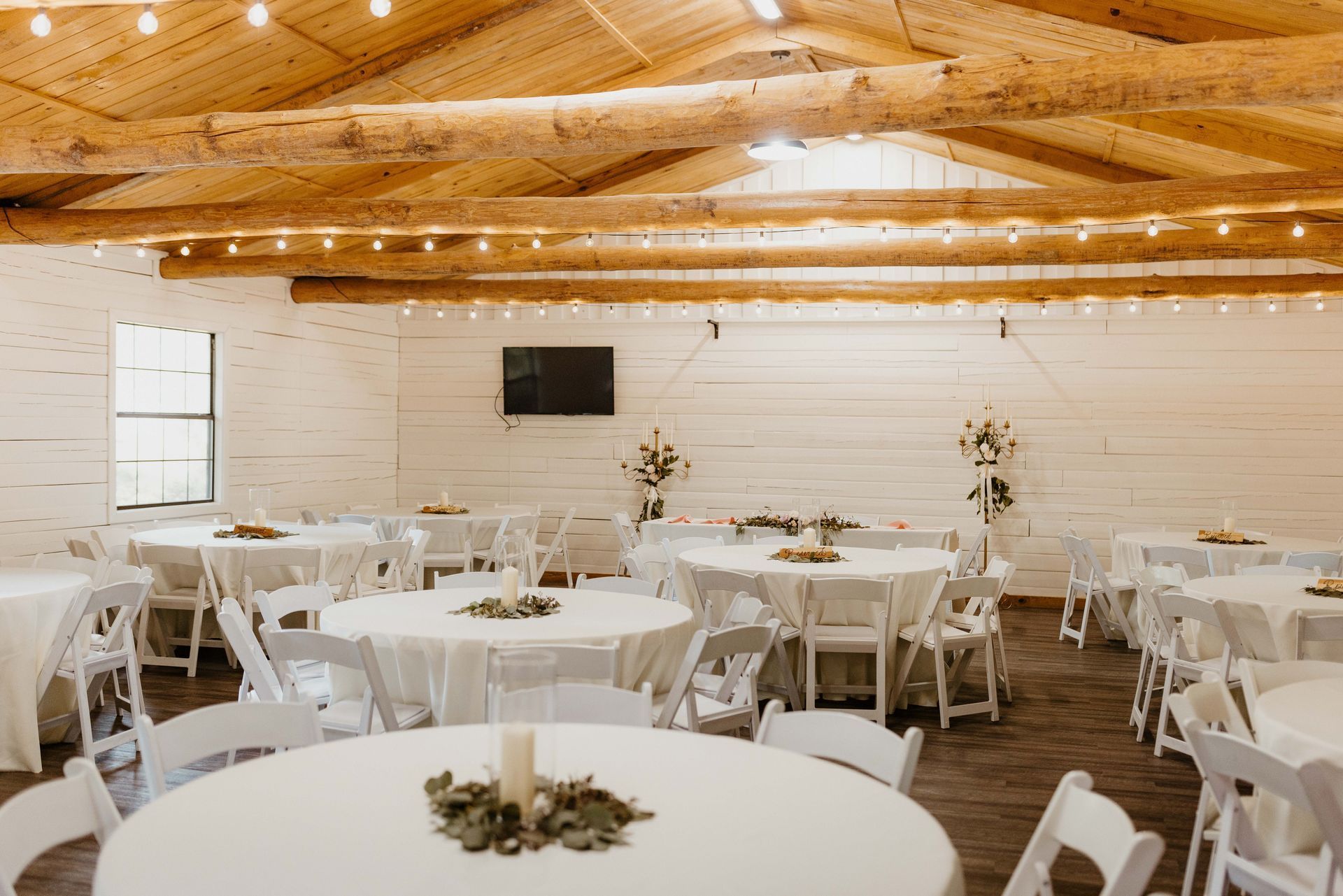A wedding reception hall with round tables covered in white linens and white folding chairs.