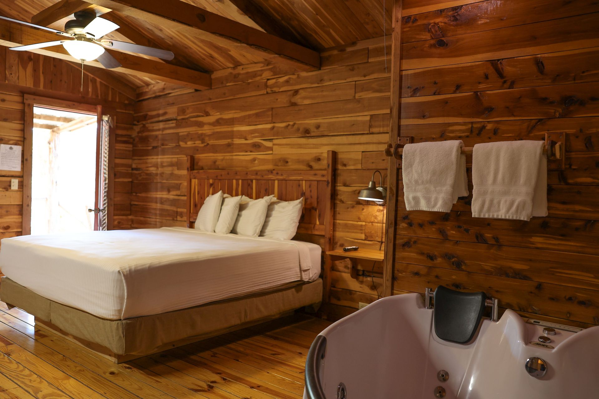 Rustic bedroom with wooden walls, a bed, and a jacuzzi tub.