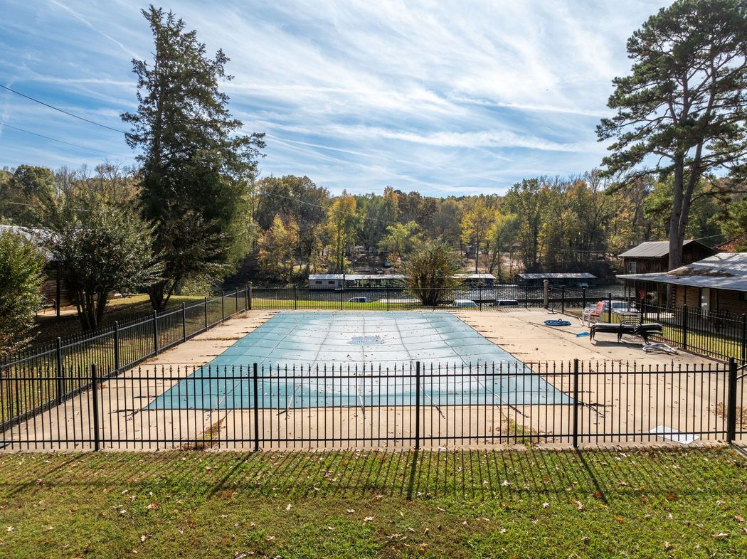 Pool covered with a blue tarp, enclosed by a black metal fence, surrounded by trees on a sunny day.