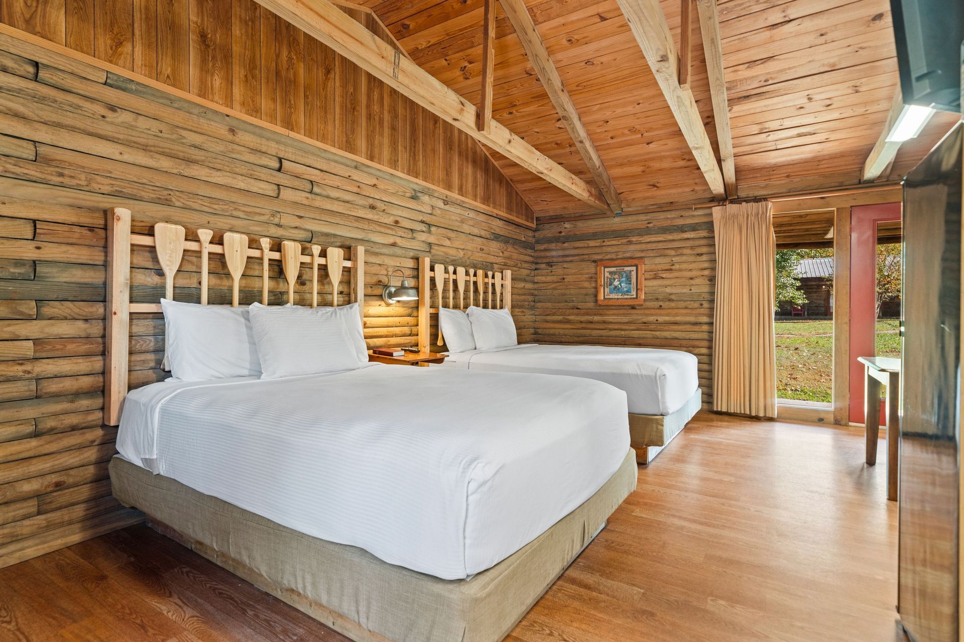 Hotel room with two beds, wooden walls and ceiling, and a doorway to outside.