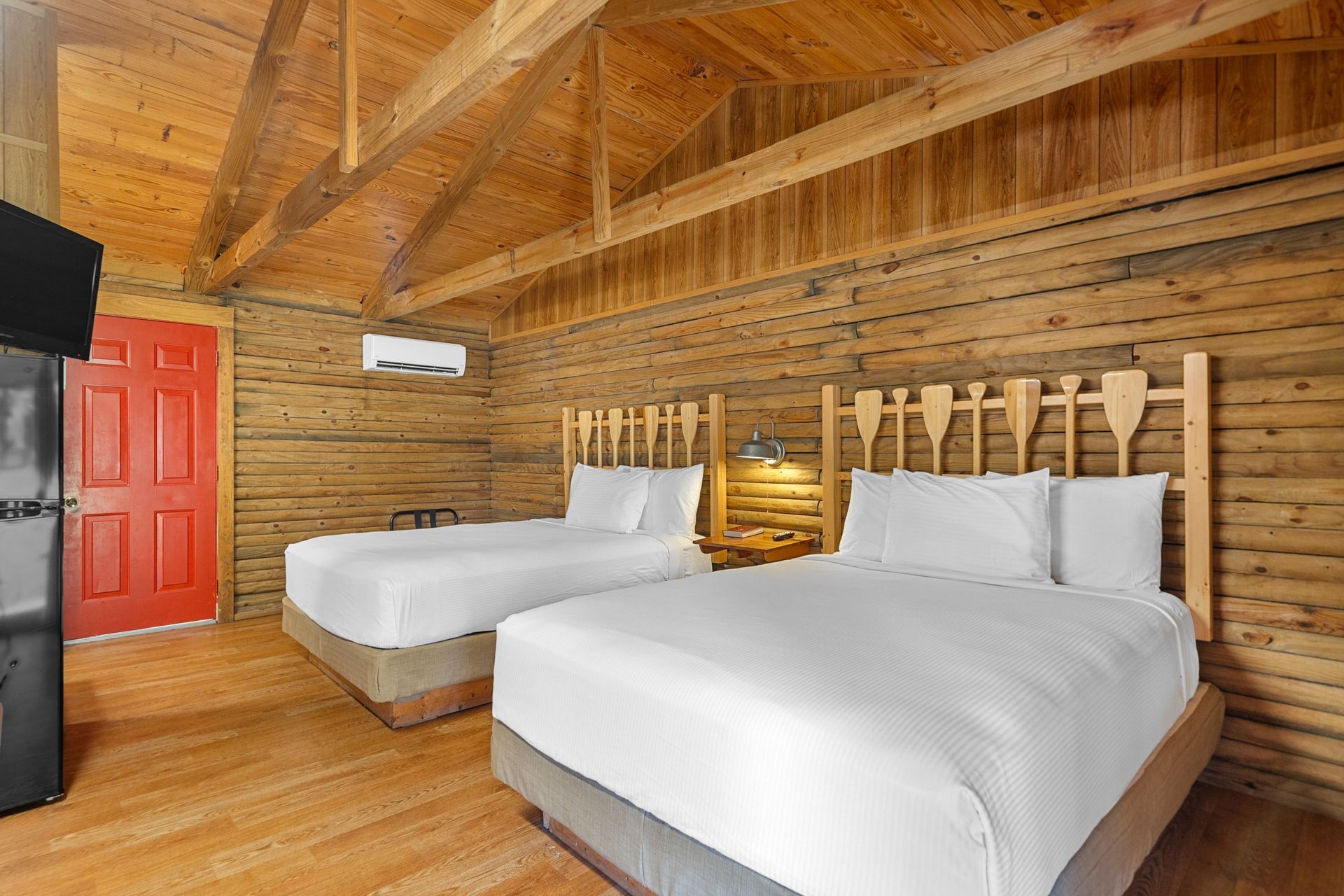 Cabin bedroom with two beds, red door, and exposed wood beams.