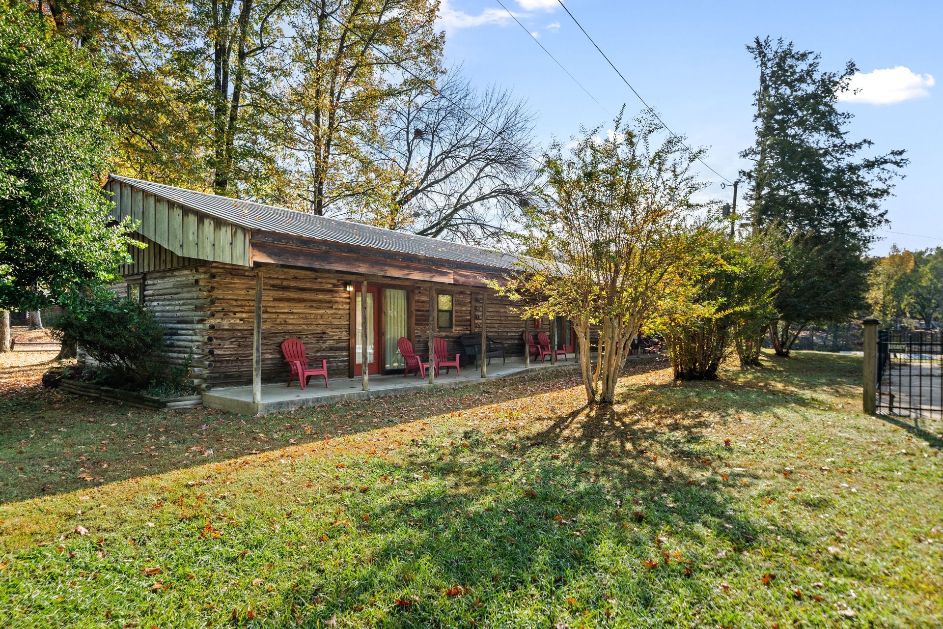 Log cabin with red chairs on porch, surrounded by trees and grass.