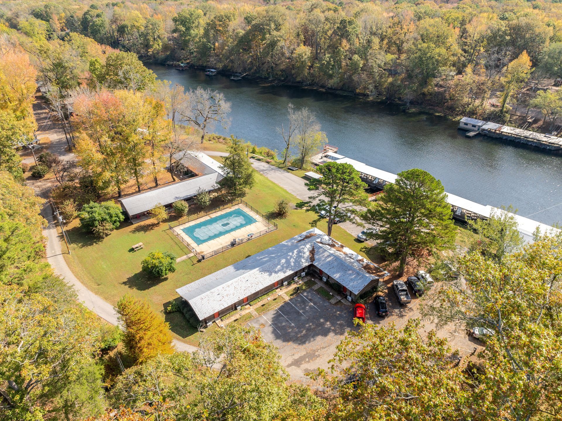 Aerial view of a motel complex beside a river. Buildings, pool, boats, trees with fall foliage.